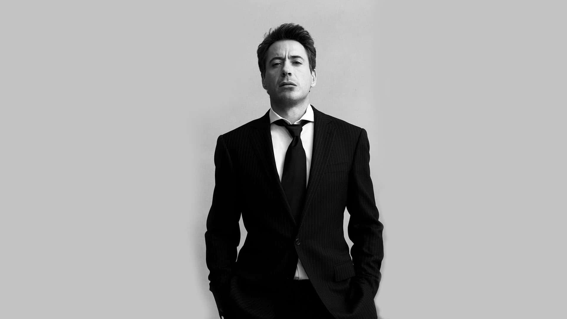 羅伯特·唐尼 Jr. 身著男裝西裝 壁紙 — 一個穿著細條紋西裝的男人站在純灰色背景前，雙手插在口袋裡的黑白肖像。
