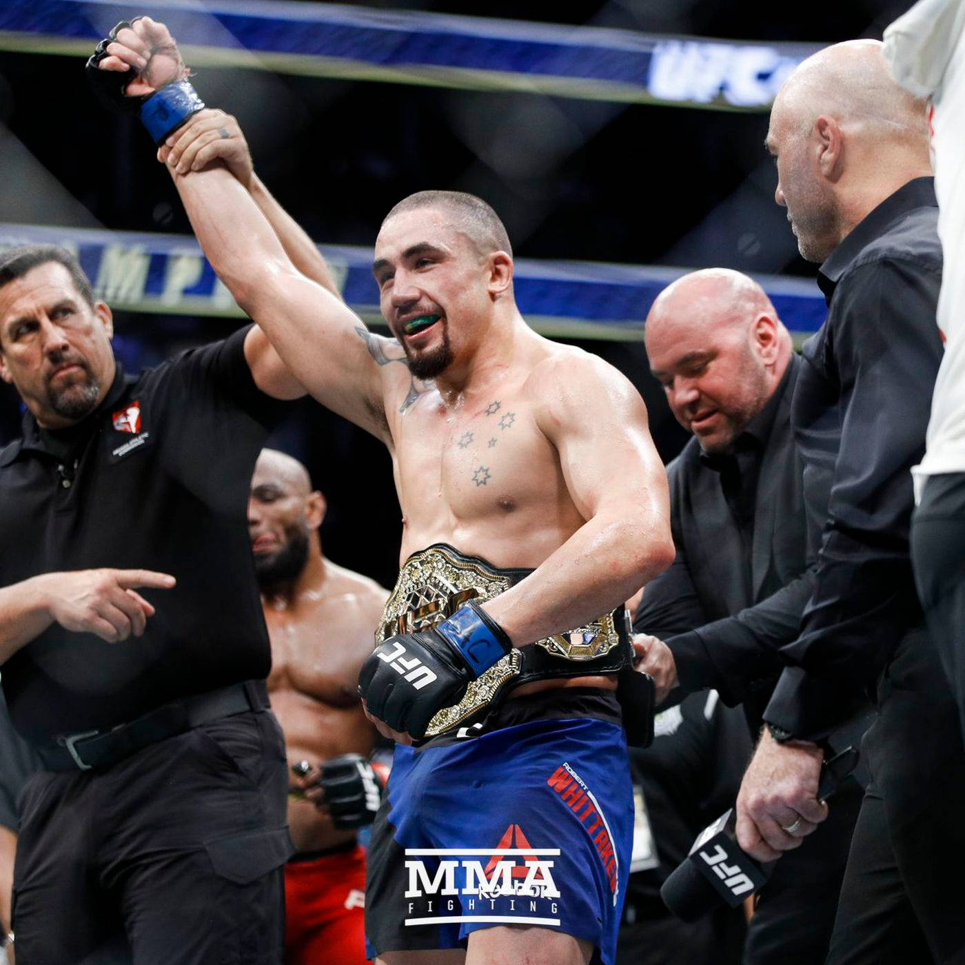 羅伯特·惠特克奪得UFC中量級冠軍 壁紙 — 一位勝利的MMA拳手在八角籠中由官員舉起手臂慶祝，同時佩戴冠軍腰帶。