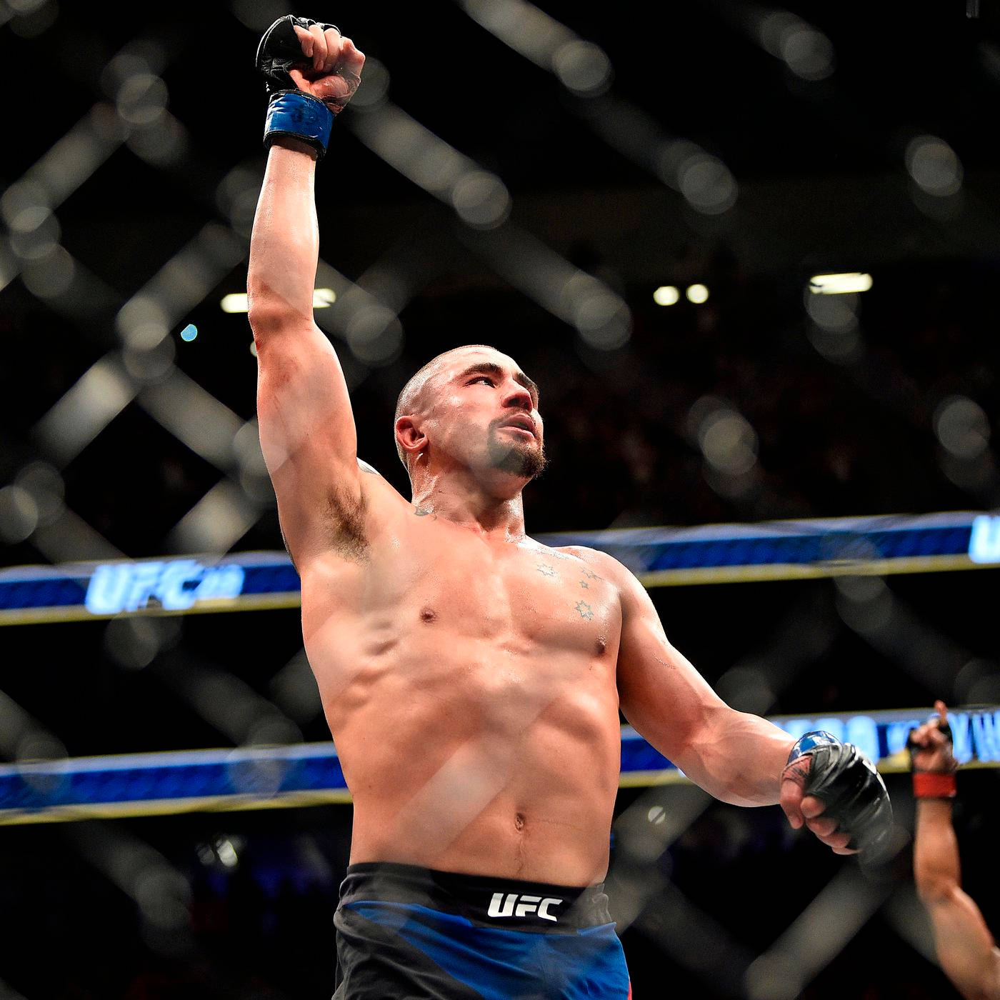 羅伯特·惠特克舉拳 壁紙 — 一位勝利的UFC拳手在明亮的場館燈光下，於八角籠內高舉拳頭慶祝勝利。