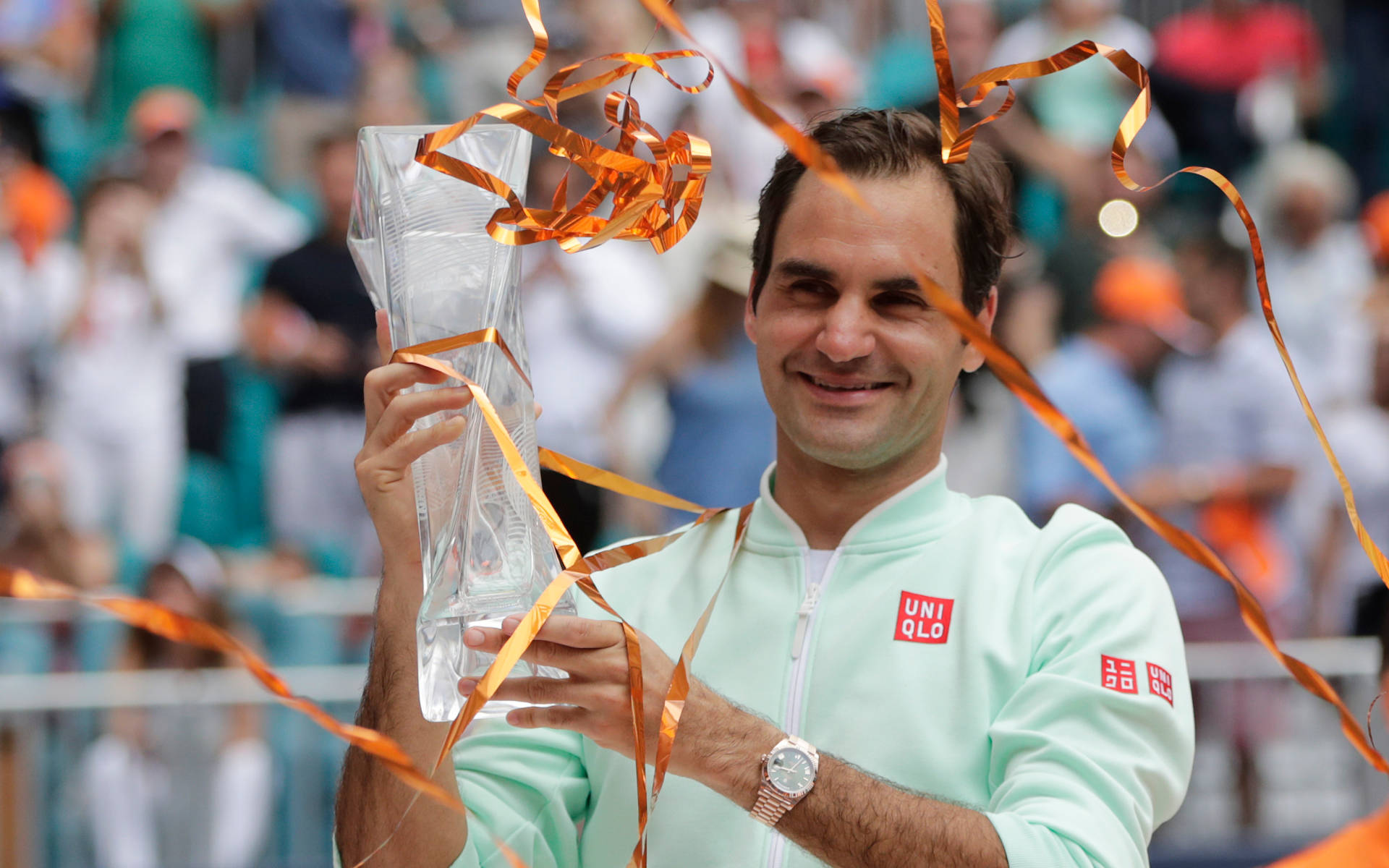羅傑·費德勒 Miami Open 網球獎盃 壁紙 — 羅傑·費達拿在網球比賽中微笑著，手持一個用橙色絲帶包裹的玻璃獎盃。