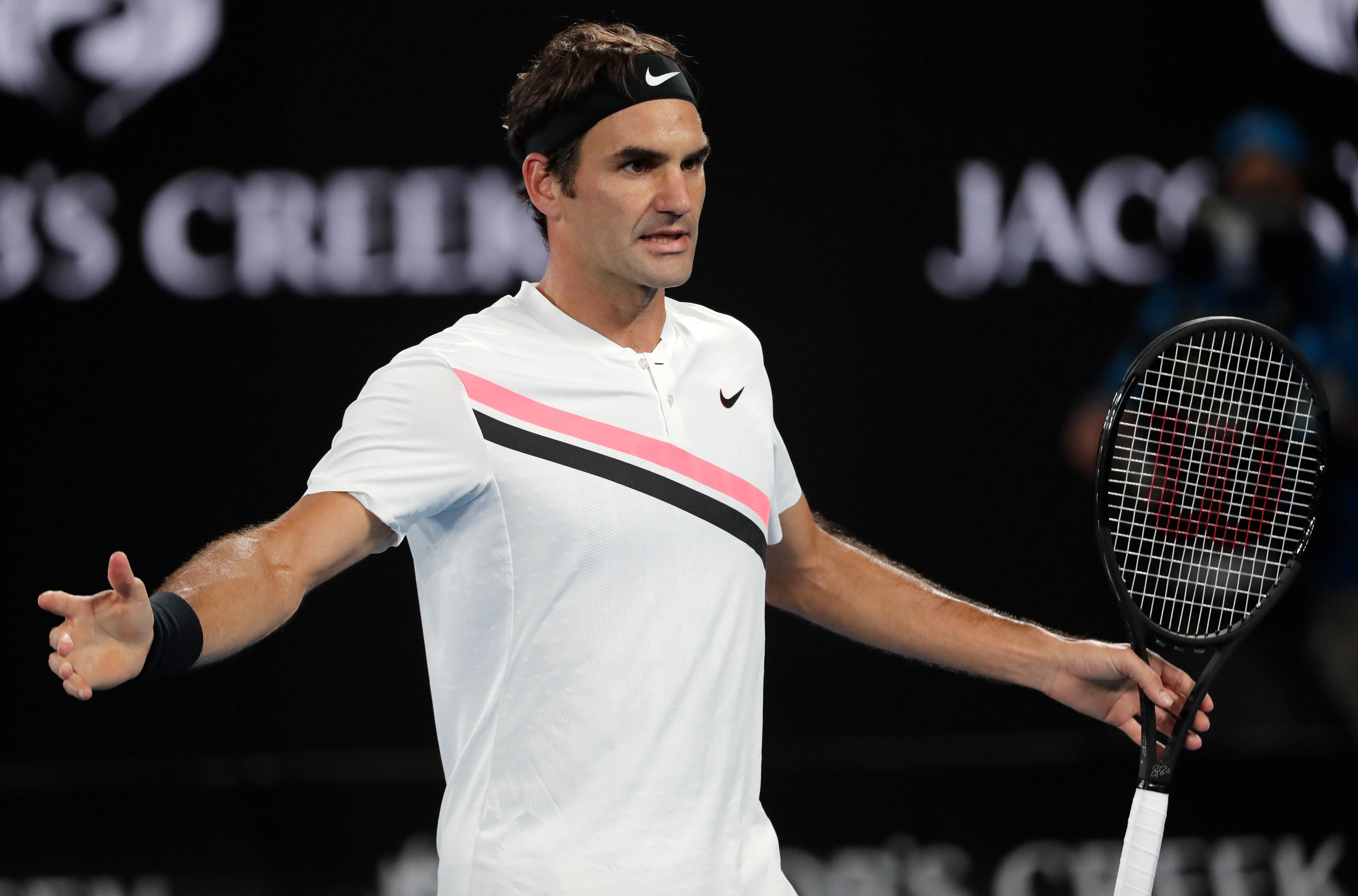 羅傑·費德勒網球運動員 壁紙 — 網球手 Roger Federer 在明亮的體育場燈光下張開雙臂握著球拍做手勢。