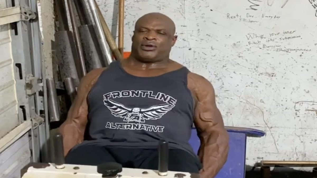 一個肌肉發達的男人坐在健身室，周圍是啞鈴和激勵人心的塗鴉。