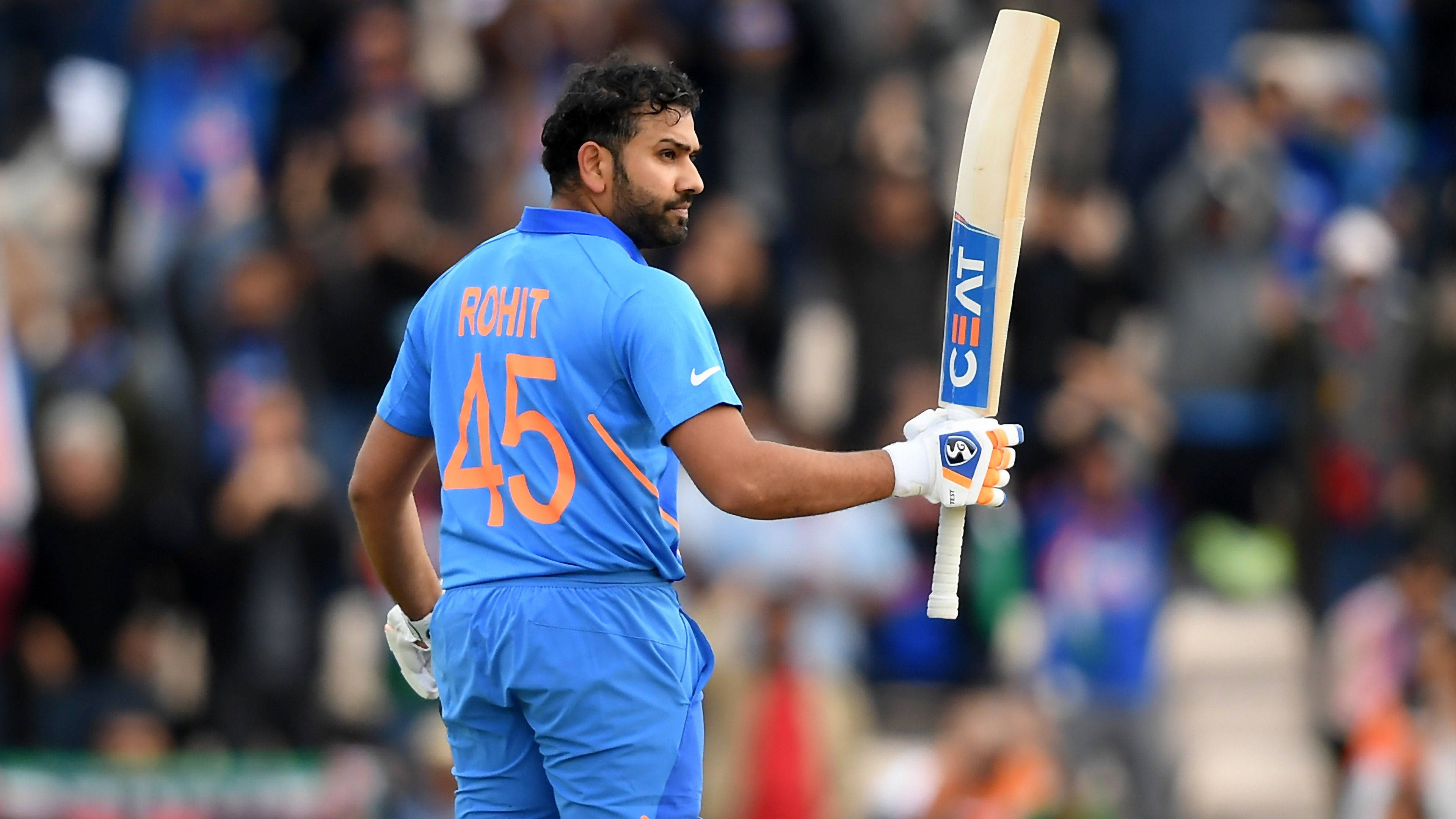 羅希特·夏爾馬板球世界杯 壁紙 — 板球運動員 Rohit Sharma 身穿藍色45號球衣，手持球棒，從體育場人群中走開。