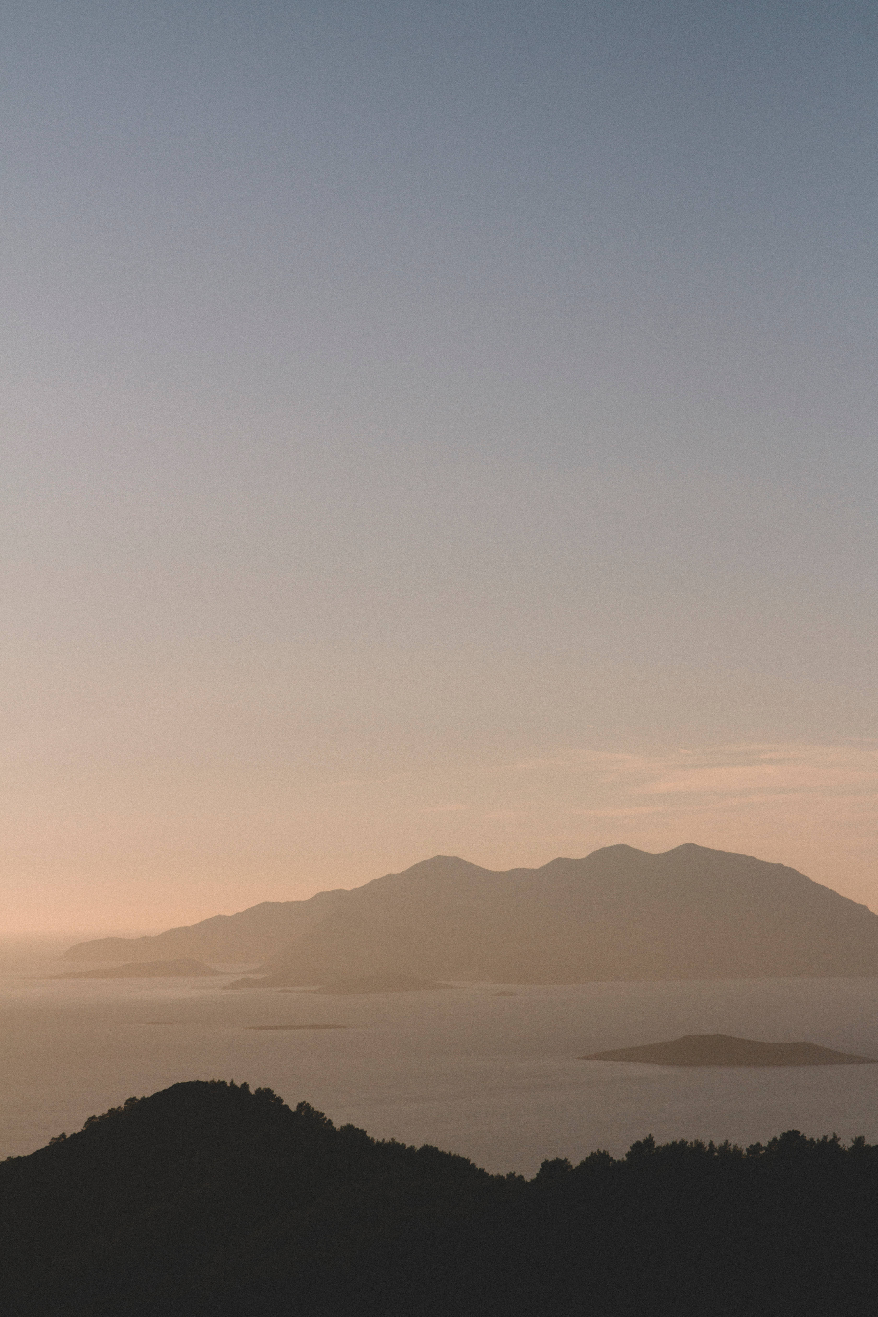 羅德島山景iOS 壁紙 — 剪影的山脈和島嶼在黎明時分柔和漸變的天空下靜靜地躺臥。