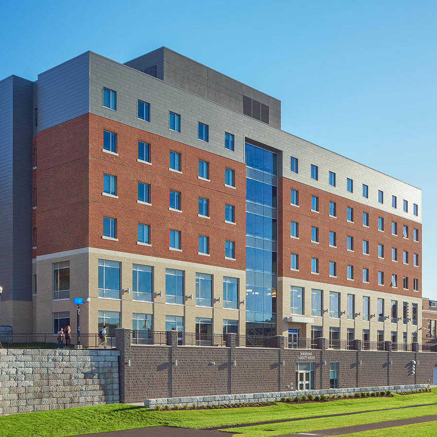 羅徹斯特大學基因廳 壁紙 — 現代多層建築，紅磚與玻璃外牆，藍天白雲下，入口附近有人群。