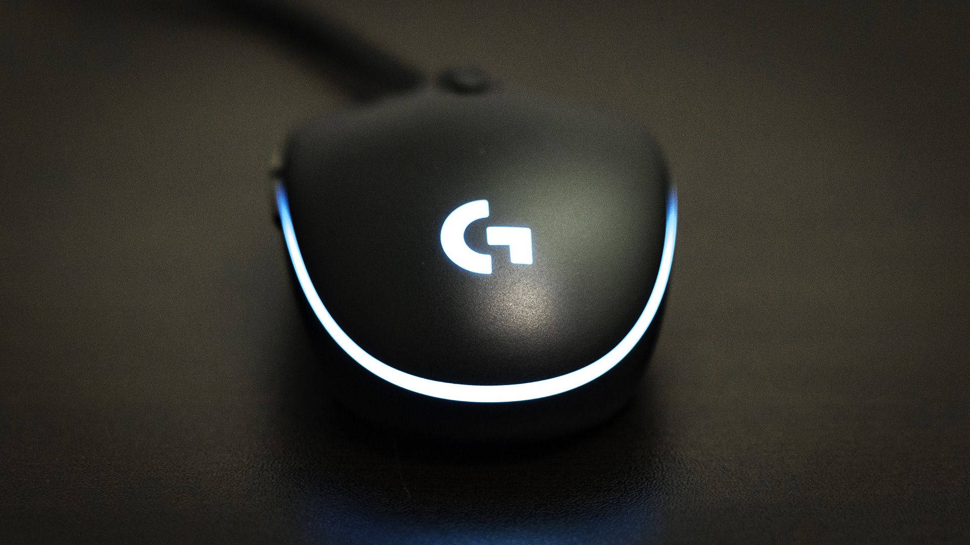 羅技帶藍光滑鼠 壁紙 — 一款時尚的黑色 Logitech 遊戲滑鼠，帶有發光的白色標誌和重點燈，放置在深色紋理表面上。