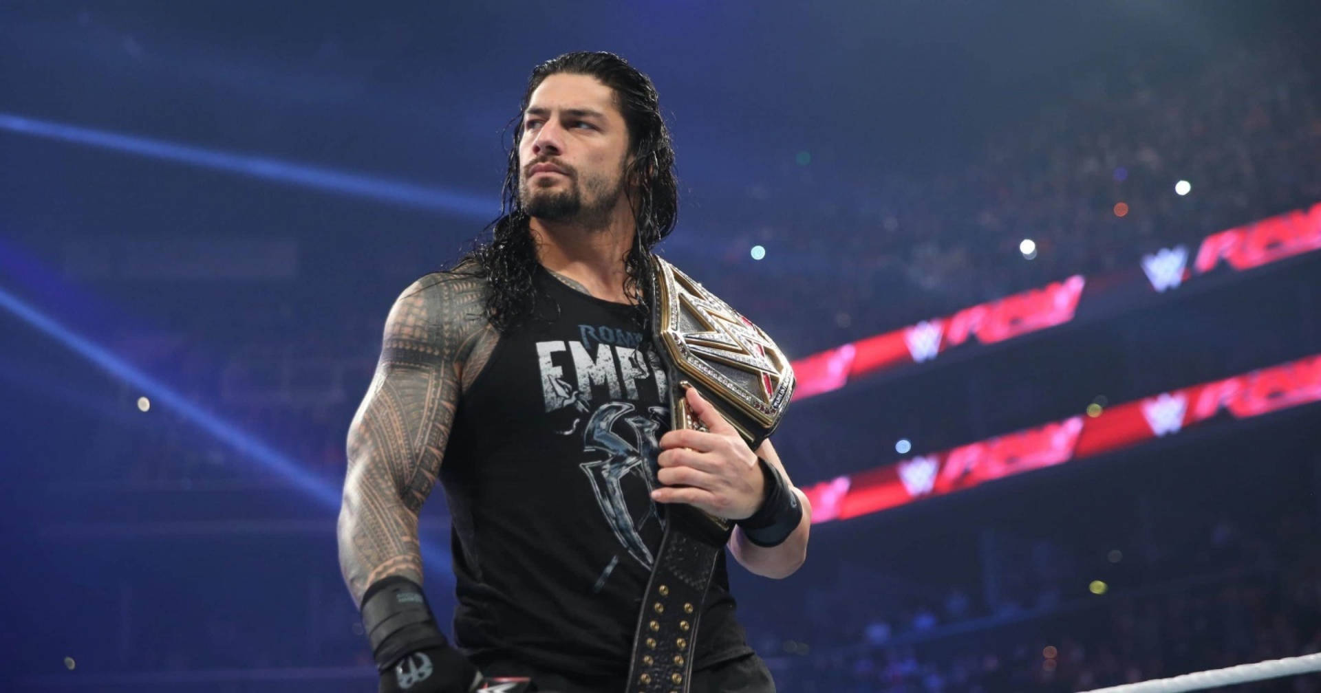 Roman Reigns 在摔角擂台上於場館燈光下手持冠軍腰帶。