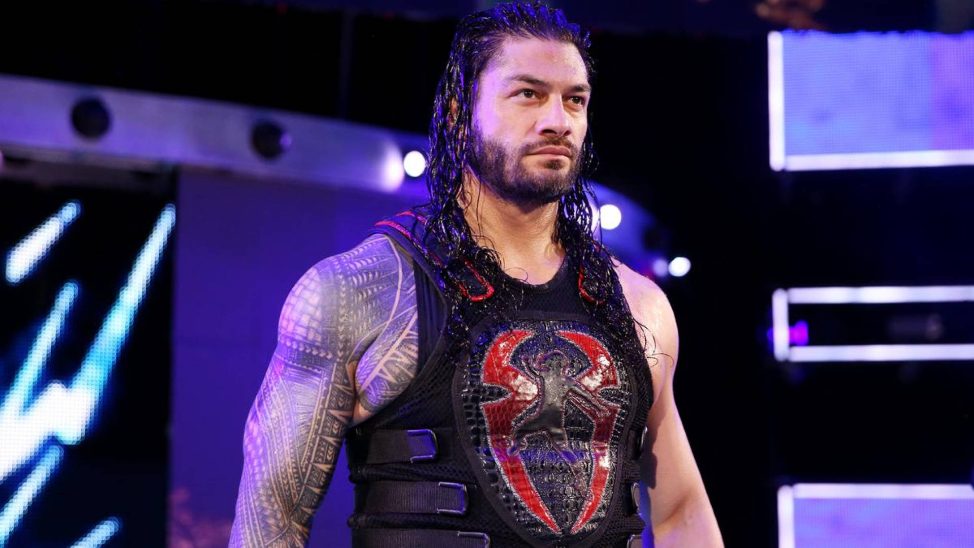 摔角手 Roman Reigns 身穿帶有紅色蜘蛛標誌的黑色背心，在紫色燈光下。