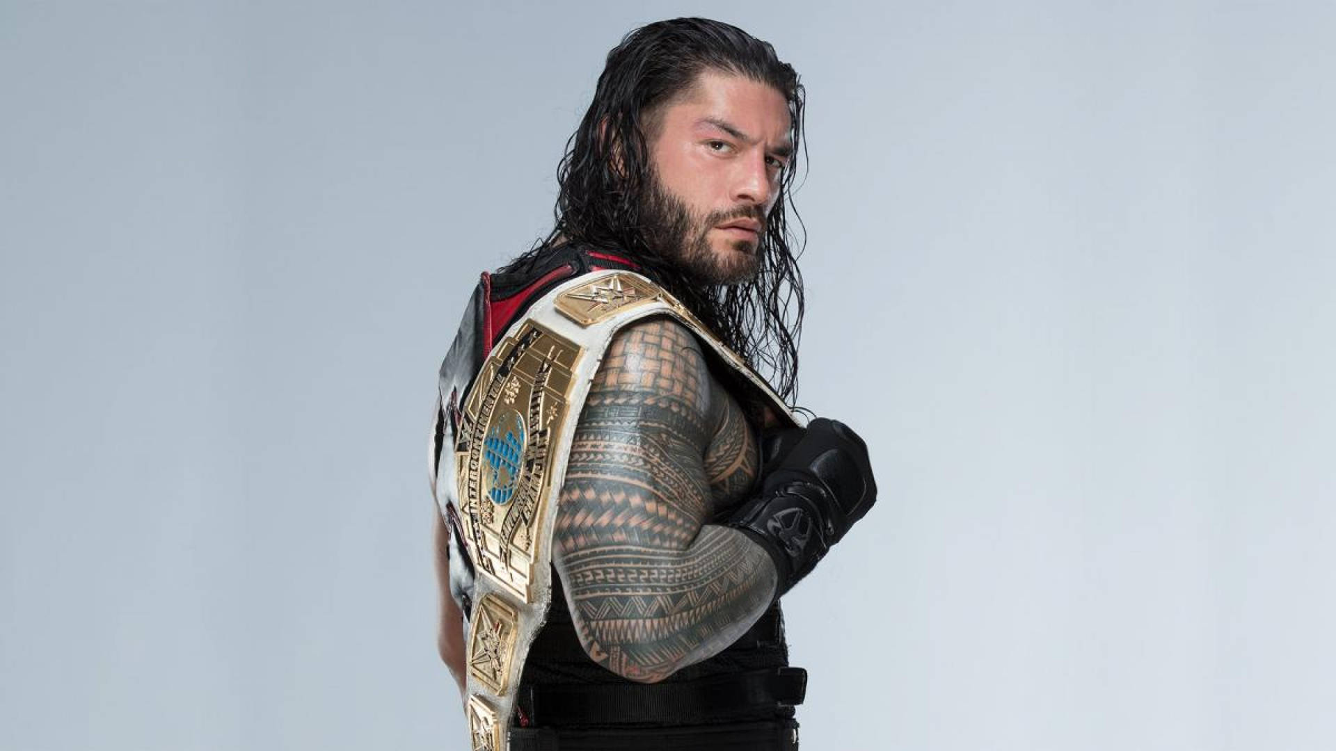 摔角手 Roman Reigns 佩戴冠軍腰帶和黑色裝備，身上有紋身。