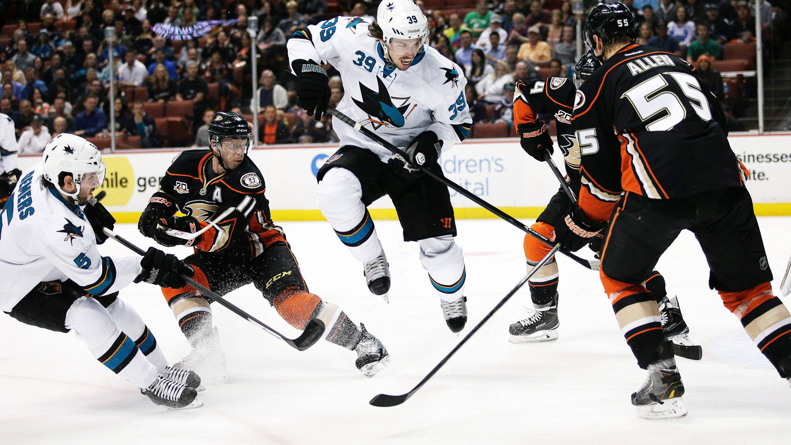羅根·庫圖爾參與 Anaheim Ducks 對決賽 壁紙 — 身穿白色和黑色球衣的冰球運動員在明亮的冰場上激烈爭奪冰球，背景有觀眾。