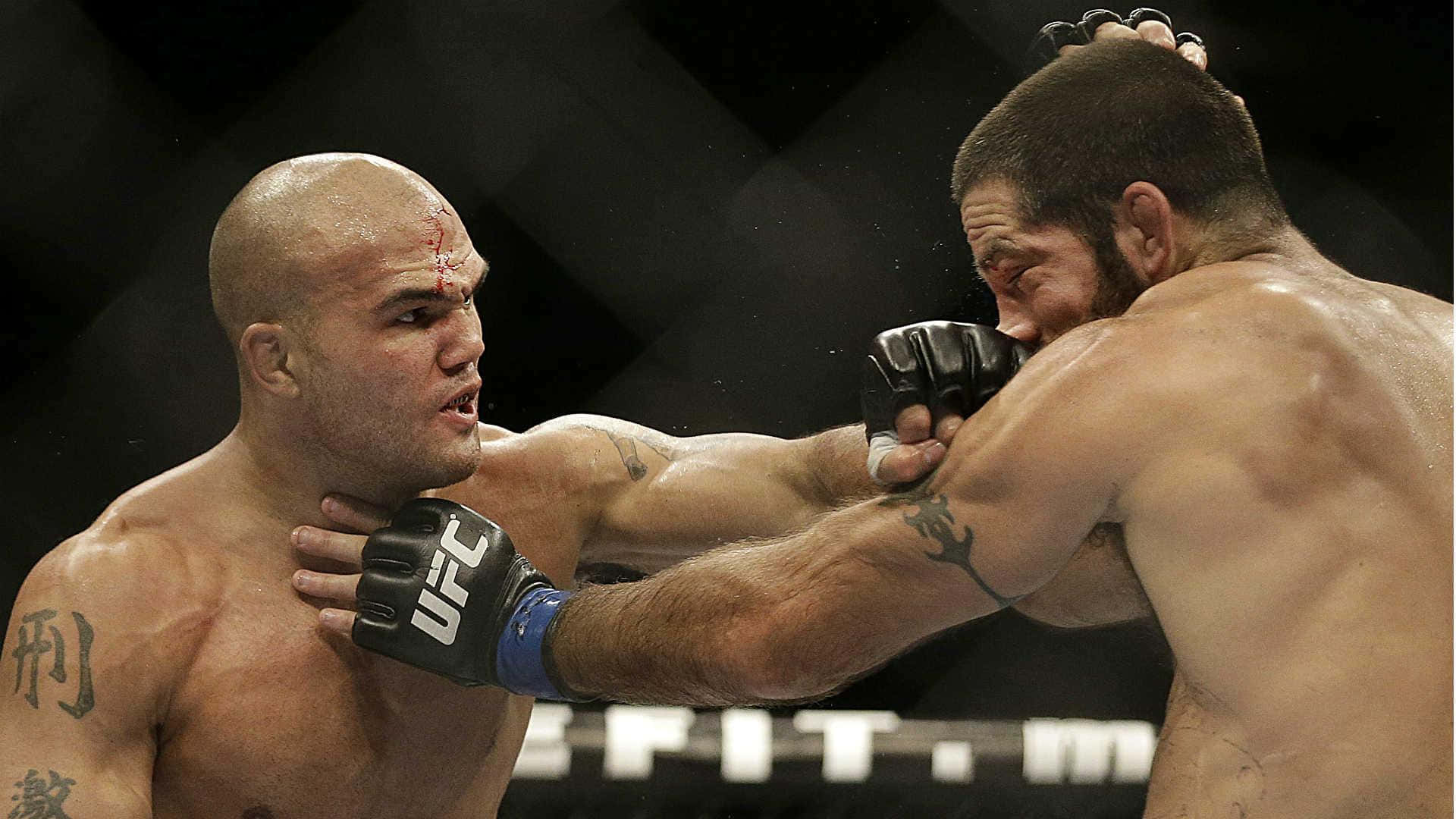 羅比·勞勒與馬特·布朗 壁紙 — 兩名肌肉發達的拳手在UFC八角籠中交鋒，其中一人打出兇猛一拳，另一人額頭流血，在明亮的場館燈光下。