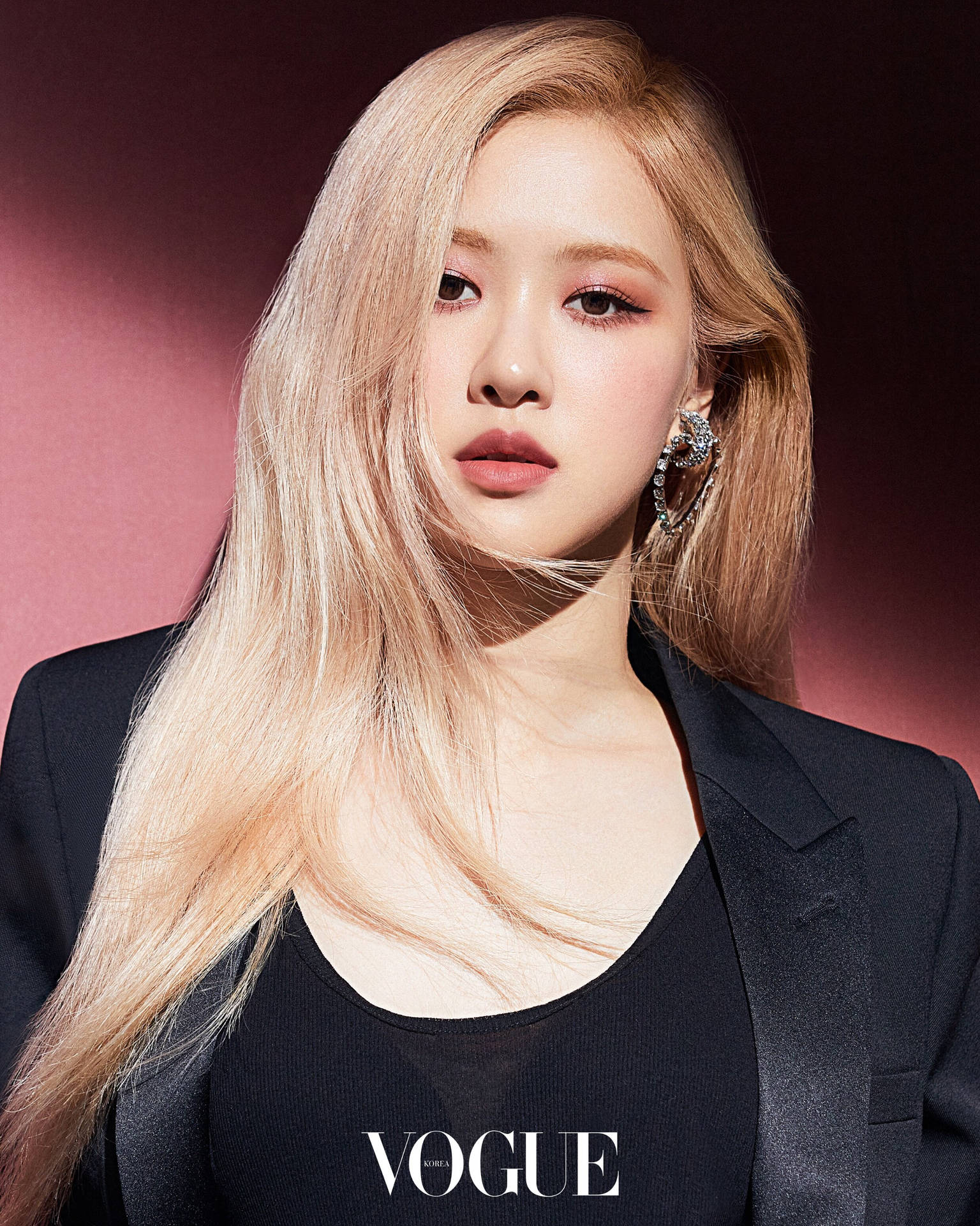 一位時尚女性，金色頭髮，穿著黑色西裝外套和Vogue標誌。
