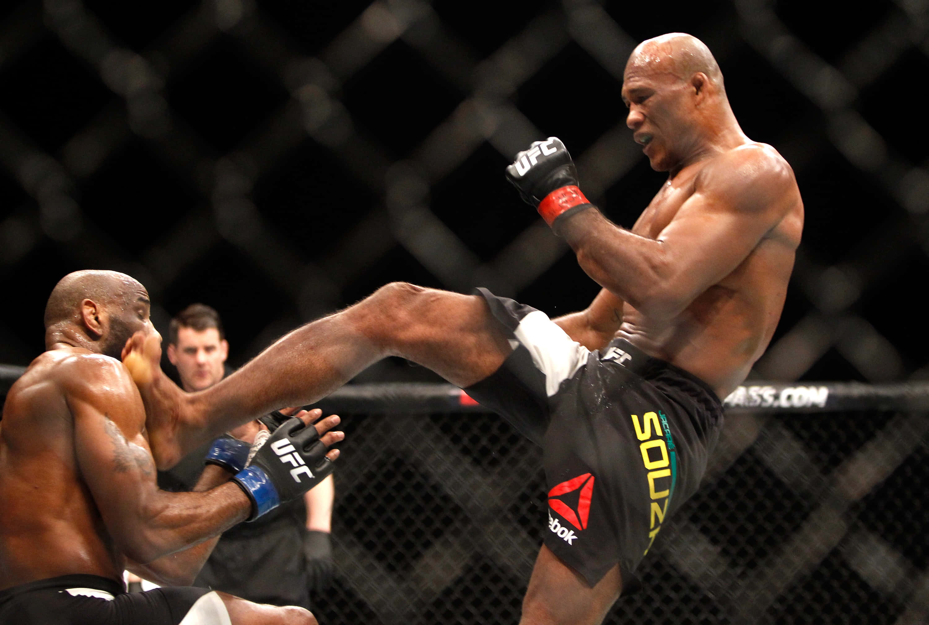 羅納爾多·蘇扎踢擊Derek Brunson 壁紙 — 一名肌肉發達的拳手在明亮的場館燈光下，於UFC八角籠內向對手踢出一記高踢。