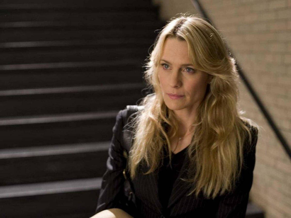 一位穿著黑色西裝外套的金髮女子表情嚴肅地坐在黑暗的樓梯上。