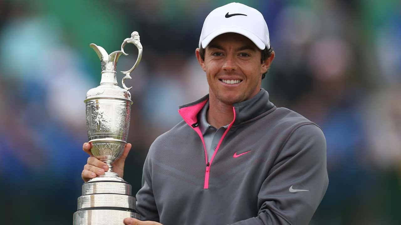 羅里·麥克羅伊手持獎盃 壁紙 — 高爾夫球手Rory McIlroy在高爾夫錦標賽中自豪地微笑，手持標誌性的銀色Claret Jug獎盃。
