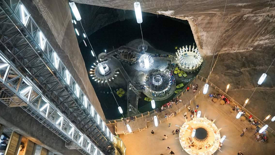 羅馬尼亞地下迷宮圖 壁紙 — 發光地下洞穴轉變為未來展覽空間的鳥瞰圖，懸掛燈光與探索圓形平台的訪客。