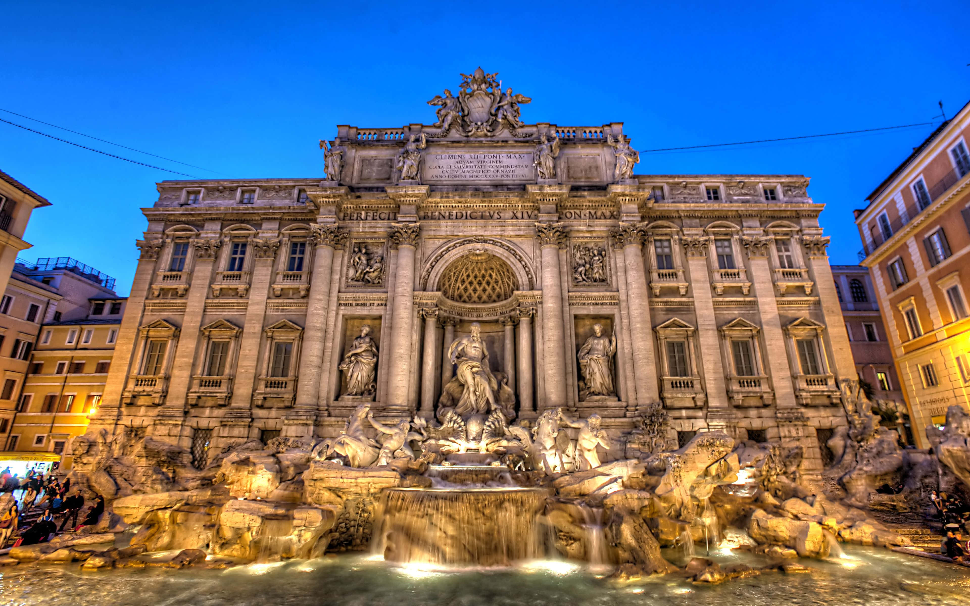 Rome 桌布 壁紙 — 羅馬的特雷維噴泉在暮色燈光下溫暖地發光，襯托著深藍色的天空，有瀑布般的水流和華麗的雕塑。