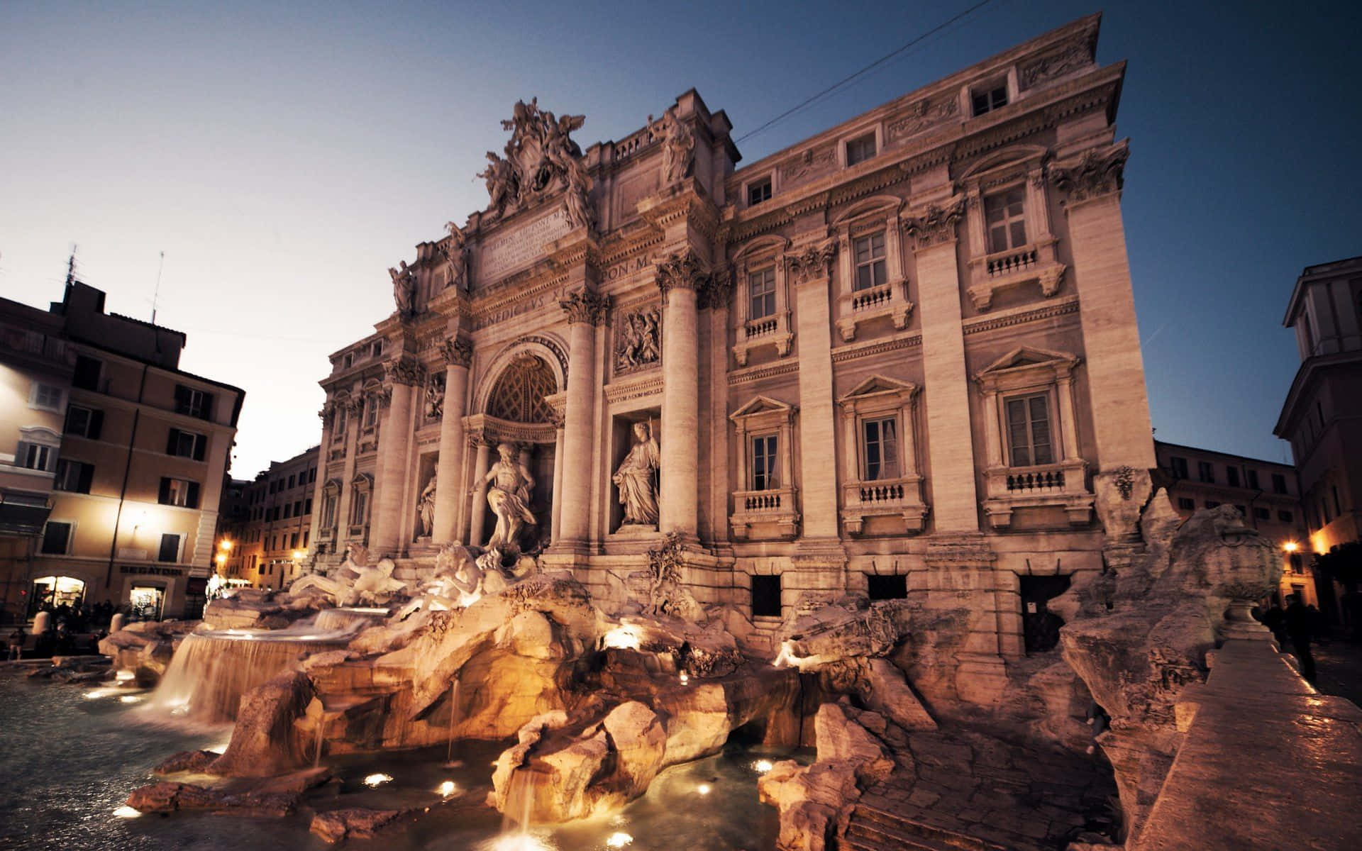 Rome 桌布 壁紙 — 羅馬的特雷維噴泉在黃昏時溫暖地發光，瀑布般的水流和燈光照亮的雕像襯托著漸深的暮色天空。
