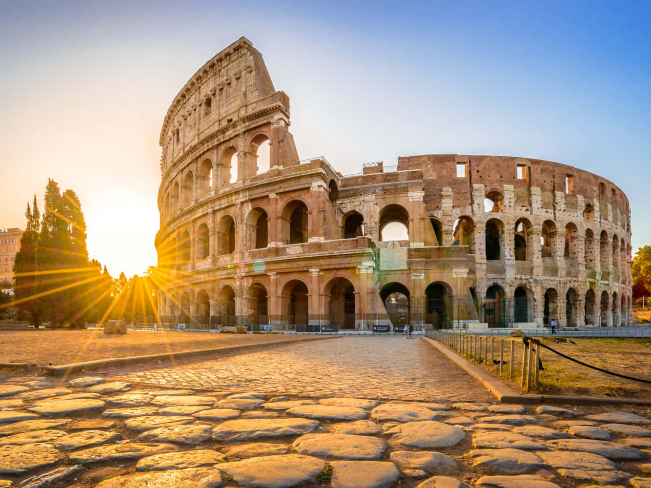 Roman 桌布 壁紙 — 羅馬競技場沐浴在金色的日出光芒中，燦爛的陽光穿過古老石拱門上方的天空。