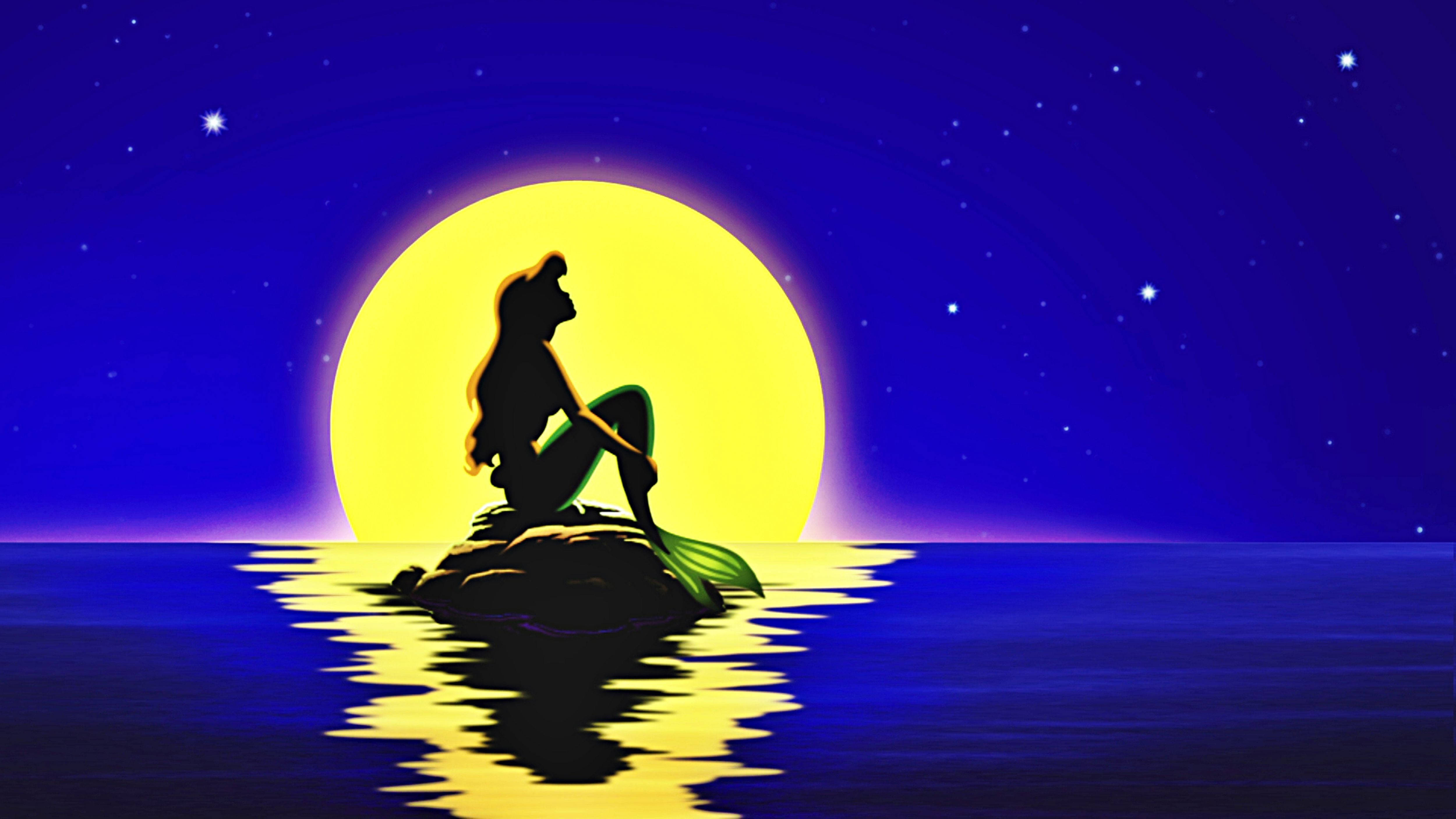 Disney Princess 桌布 壁紙 — 美人魚剪影坐在岩石上，凝視著星光燦爛的深藍色夜空中的一輪發光的黃色月亮。
