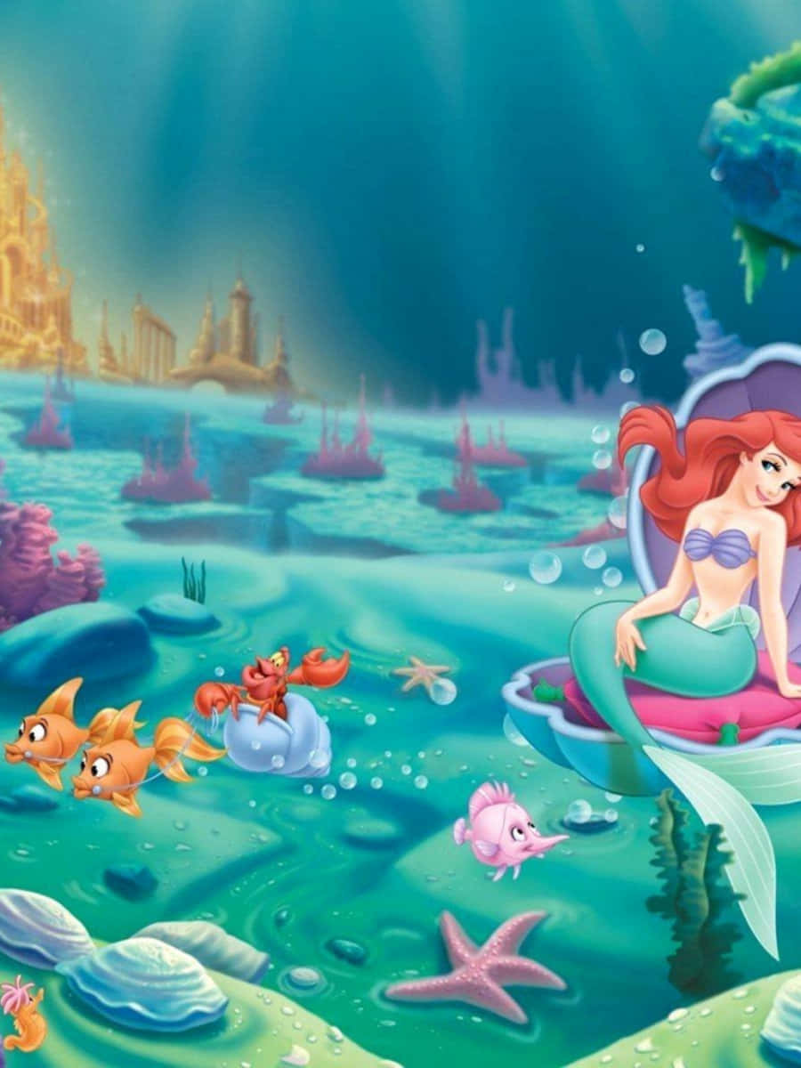 Kawaii Mermaid 桌布 壁紙 — 美人魚艾莉爾坐在水中的貝殼寶座上，與她的朋友們（包括小比目魚和賽巴斯丁）一起，附近有陽光照射的珊瑚礁和遠處的城堡。