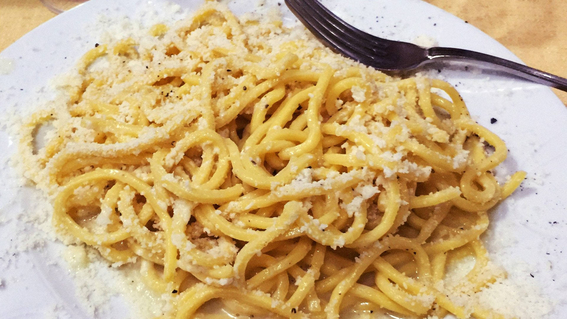 美味 Cacio E Pepe 壁紙 — 忌廉意粉配磨碎芝士和黑胡椒的特寫，放在有斑點的白色碟上，附有叉子。