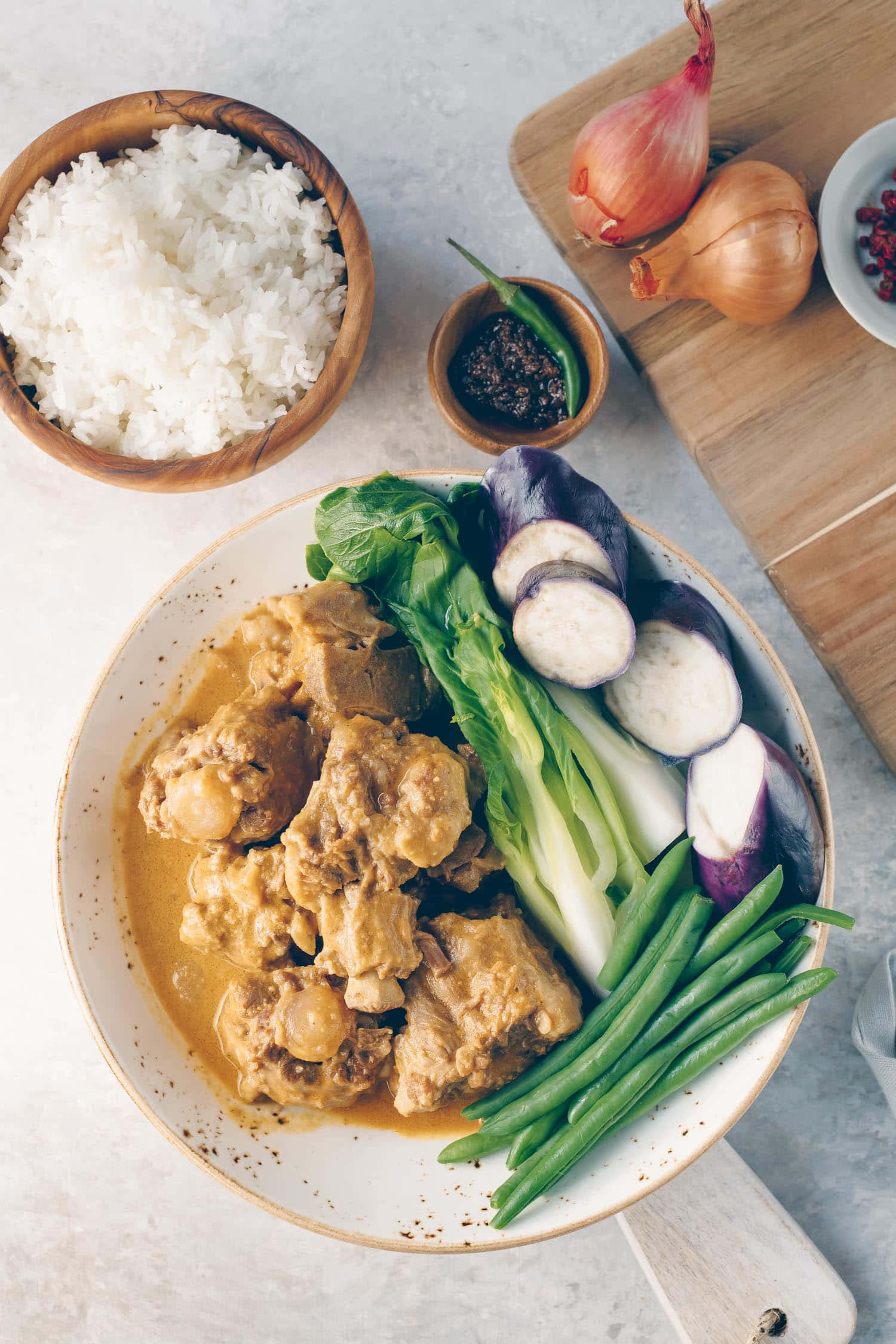 美味咖喱牛尾湯配白飯——菲律賓美食之樂趣 壁紙 — 從上方俯瞰一個豐盛的咖哩菜餚，有雞肉和蔬菜，配上白飯和新鮮食材，放在木板上。