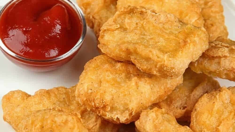 美味多汁的雞塊 壁紙 — 金黃酥脆的雞塊高高堆起，旁邊放著一小碗鮮紅色的番茄醬，置於白色碟子上。