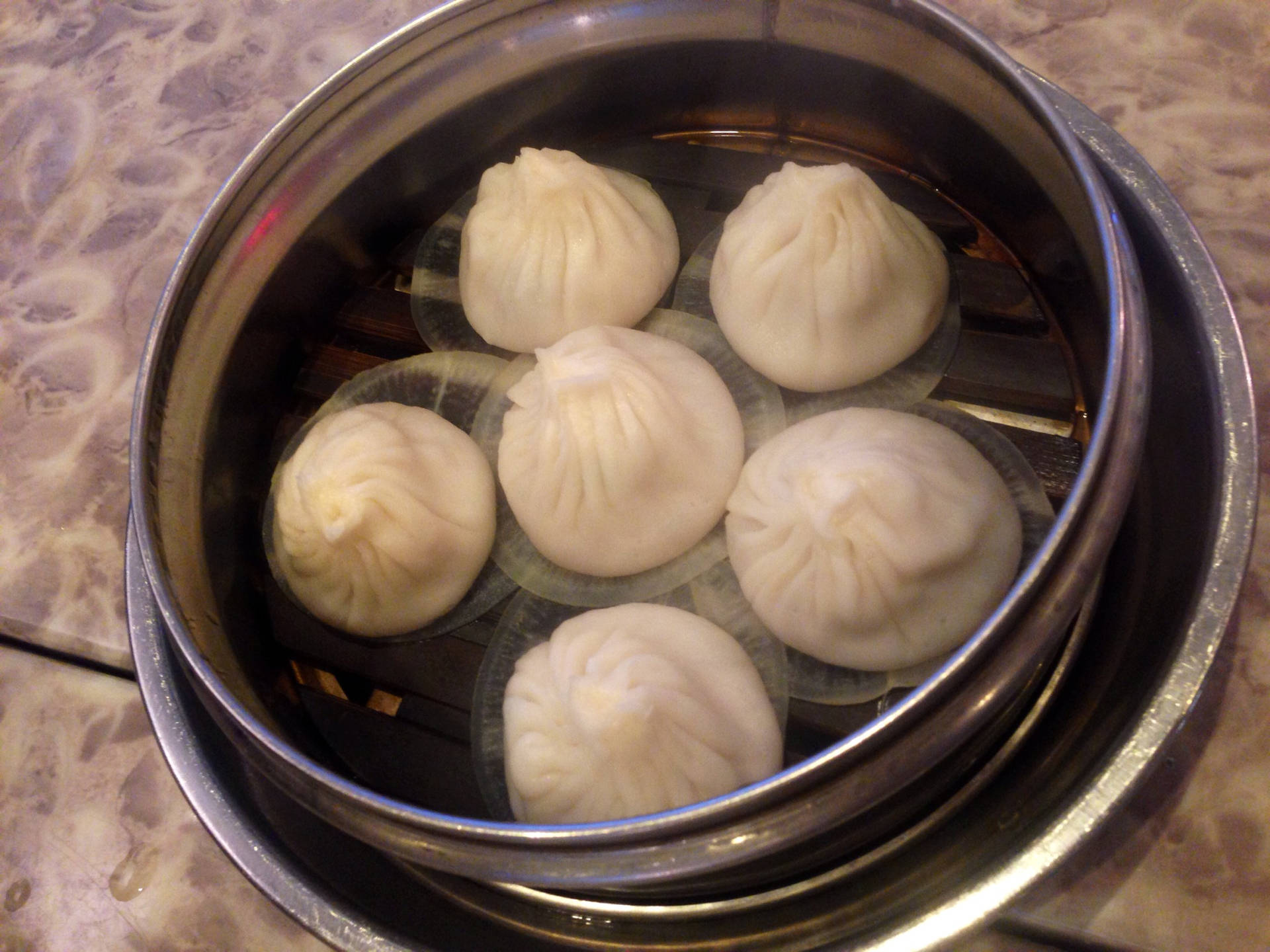 金屬蒸籠裡的六個蒸餃，放在有圖案的表面上。
