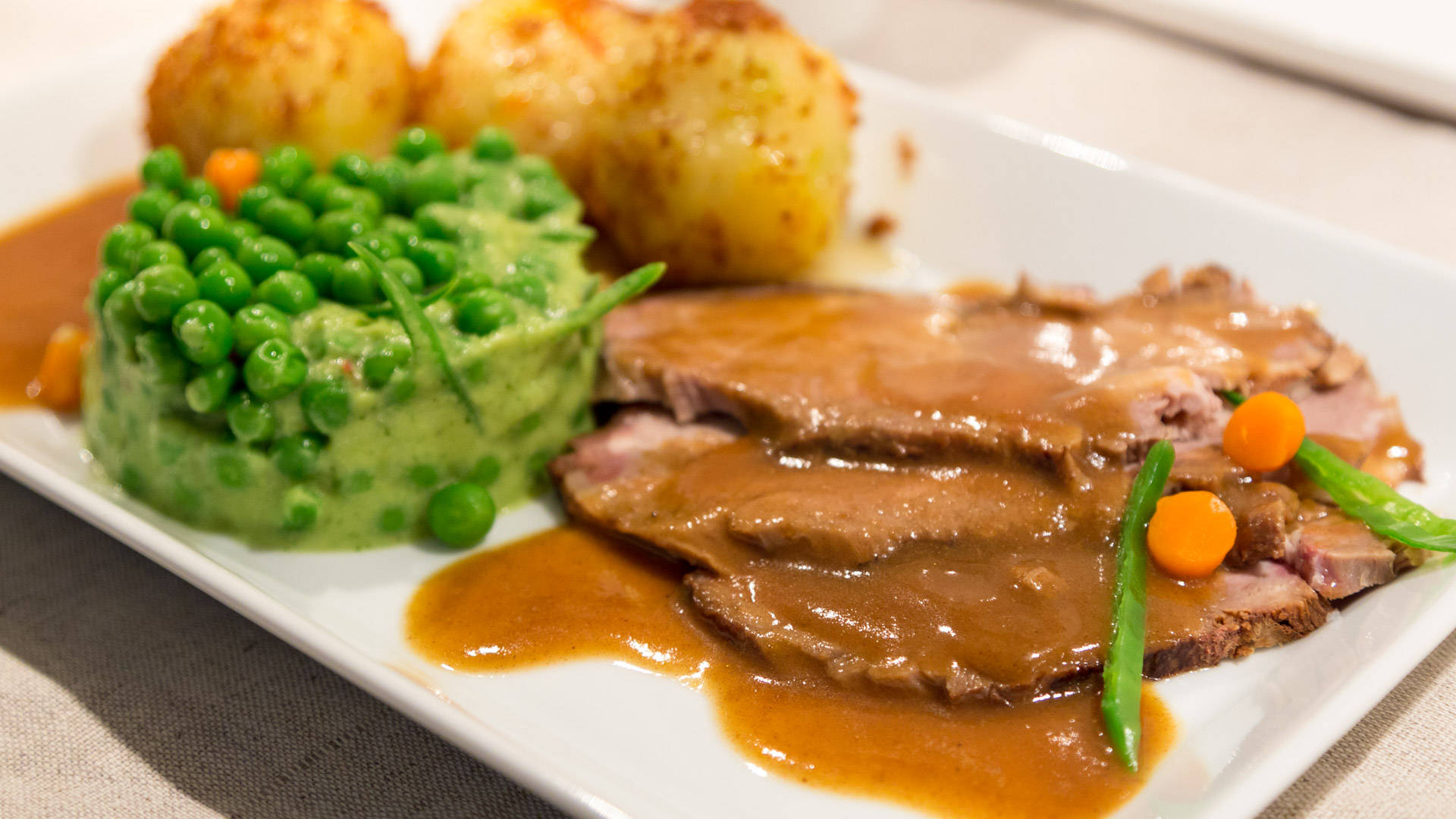 切片烤牛肉配肉汁、豌豆和馬鈴薯，盛在白色盤子上。