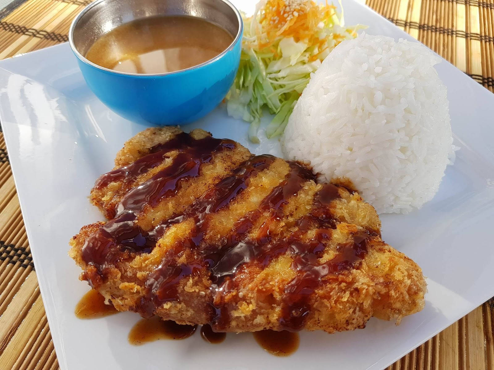 美味日式炸豬排 - 酥脆豬肉排 壁紙 — 脆皮炸雞配深色醬汁，旁邊放著一堆白飯和椰菜絲，放在白色碟上。