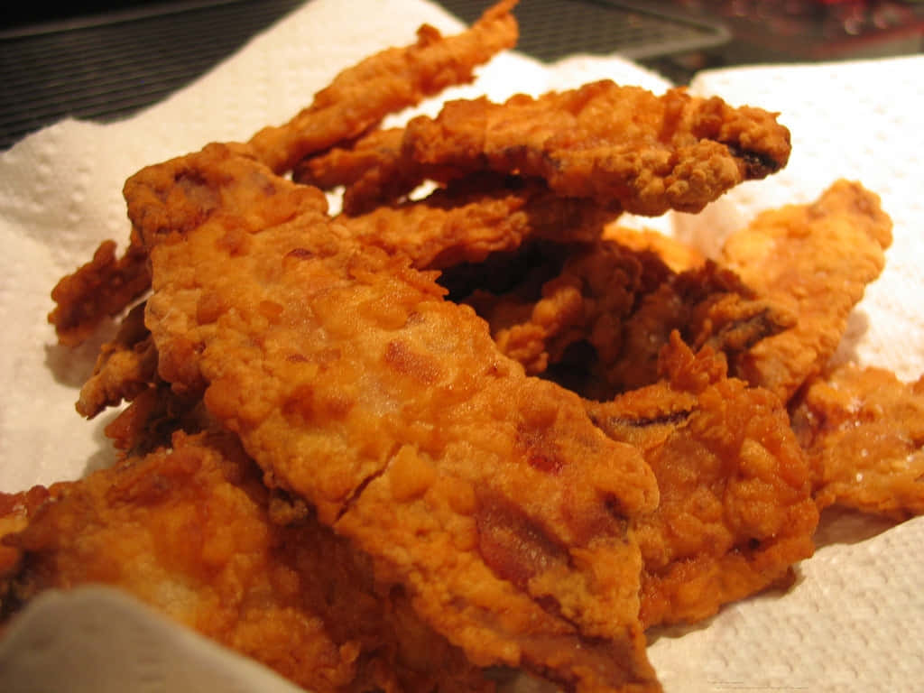 美味油炸美食拼盤 壁紙 — 金黃酥脆的炸魚條高高堆放在帶有紋理表面的白色紙巾上。