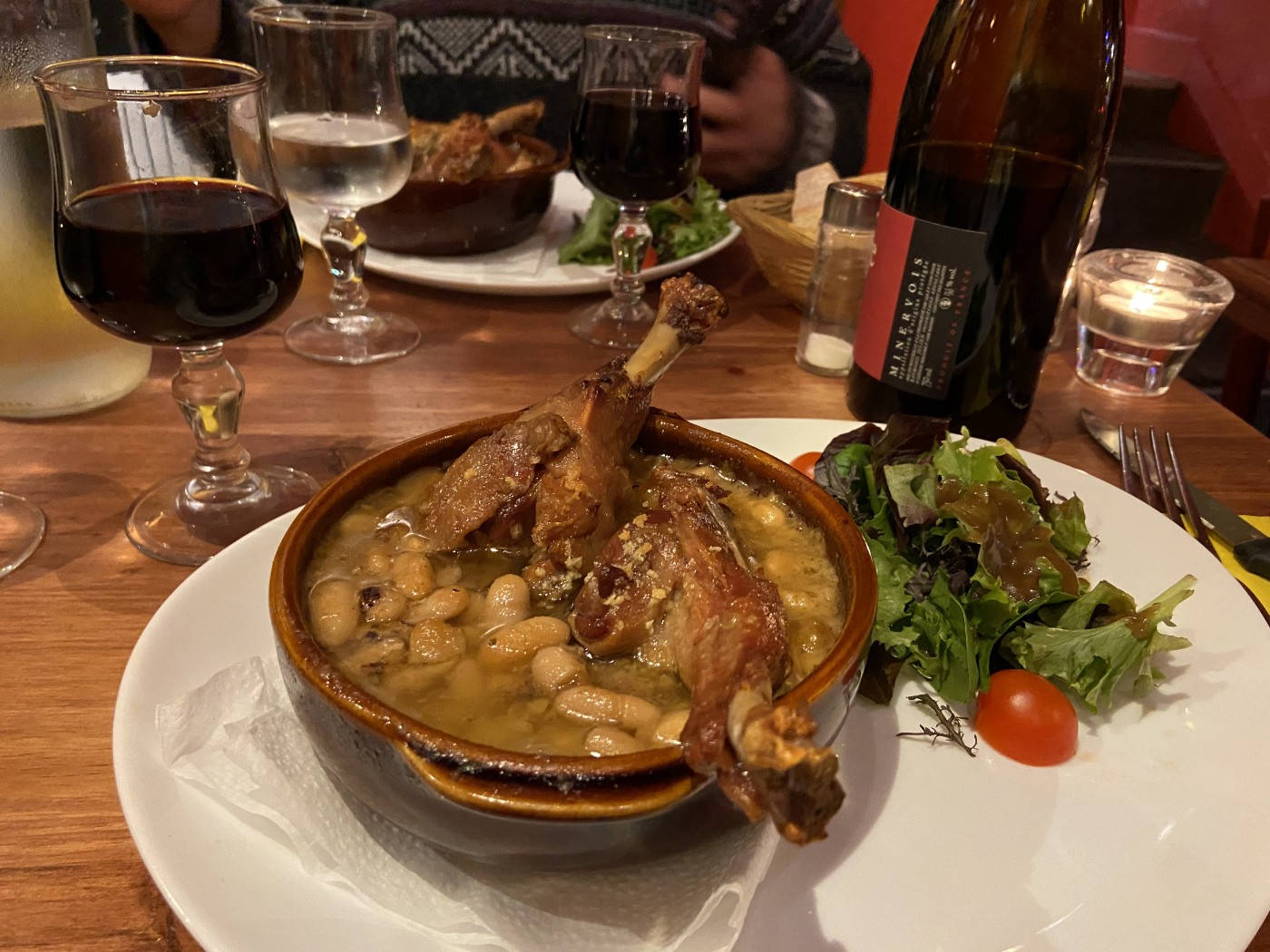 一道豐盛的雞肉白豆燉菜，配上沙律和葡萄酒，放在木桌上。