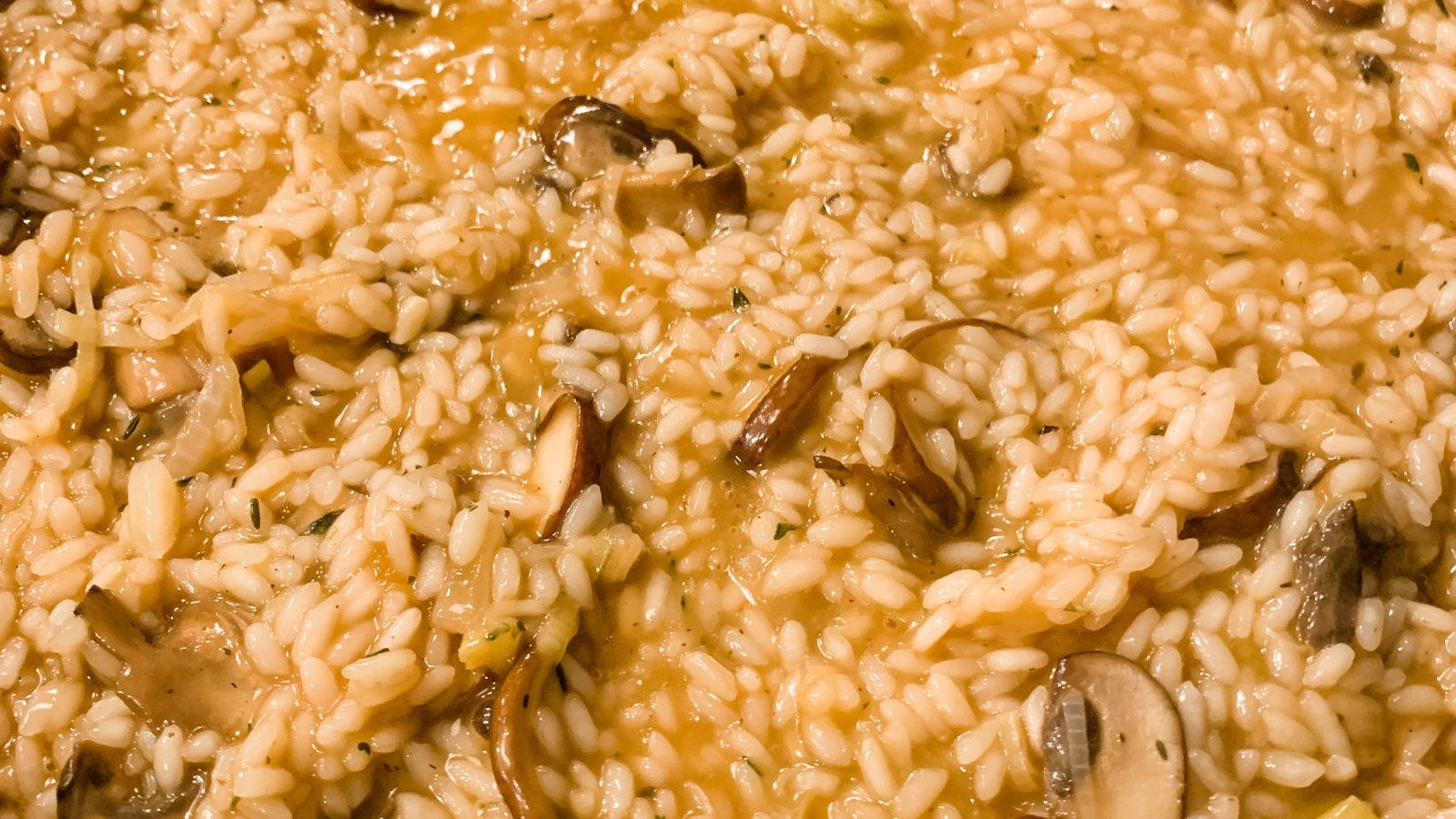 美味洋菇燉飯，經典義式料理 壁紙 — 奶油蘑菇燴飯近鏡，配以金黃高湯和新鮮香草，在溫暖燈光下閃閃發光。