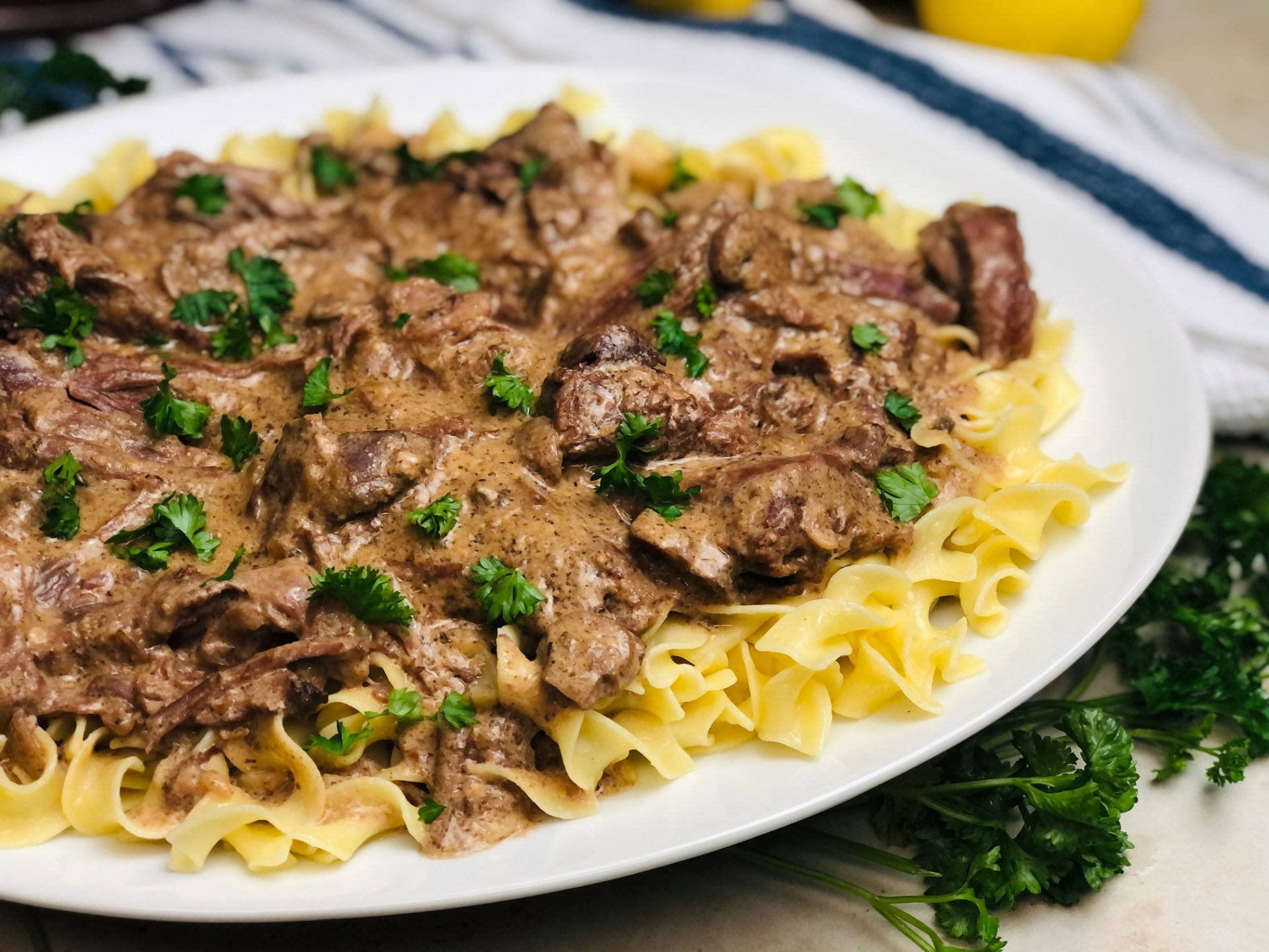 美味牛肉斯特羅甘諾夫配雷吉內特麵 壁紙 — 一盤豐富的牛肉斯特羅加諾夫配雞蛋麵，上面撒上新鮮歐芹，放在條紋布上。