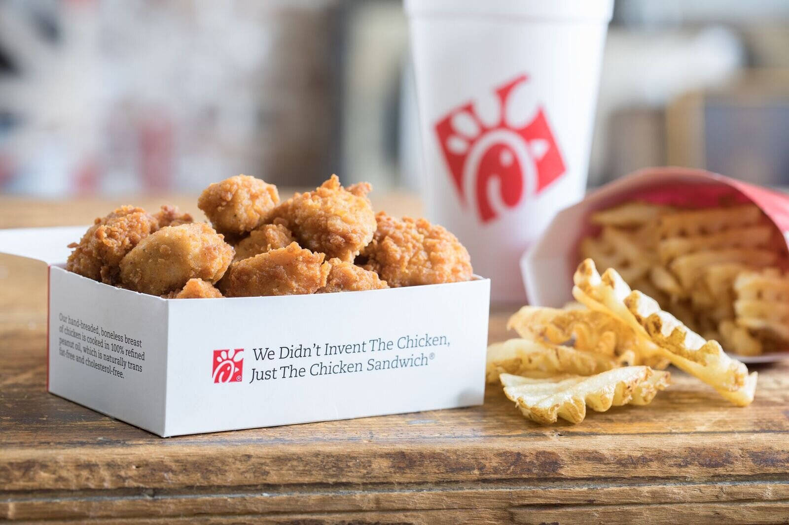 美味的 Chick Fil A 雞塊 壁紙 — 香脆炸雞塊和窩夫薯條放在一個質樸的木桌上，旁邊有一個Chick-fil-A飲料杯。