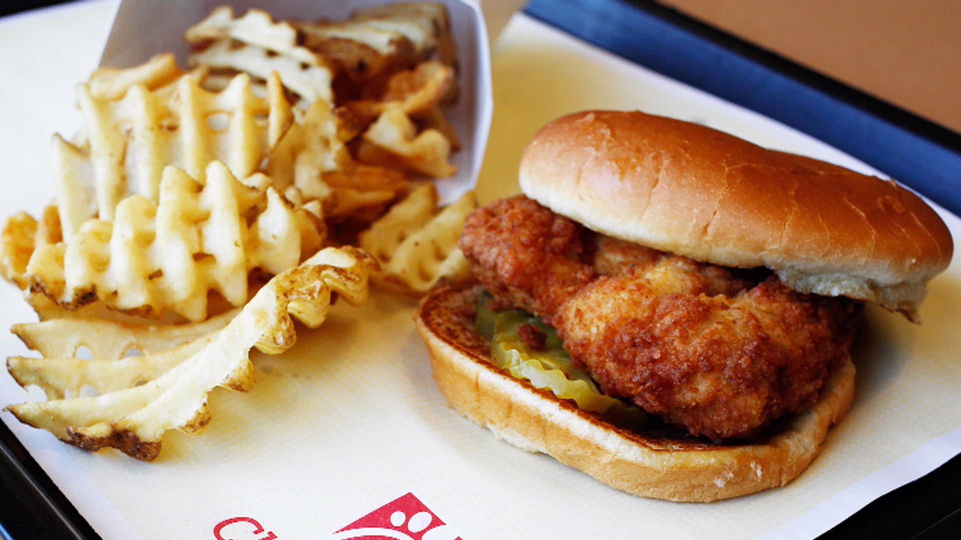 美味的 Chick Fil A 雞肉三明治 壁紙 — 金黃炸雞三文治配酸瓜及窩夫薯條，置於品牌紙托盤上。