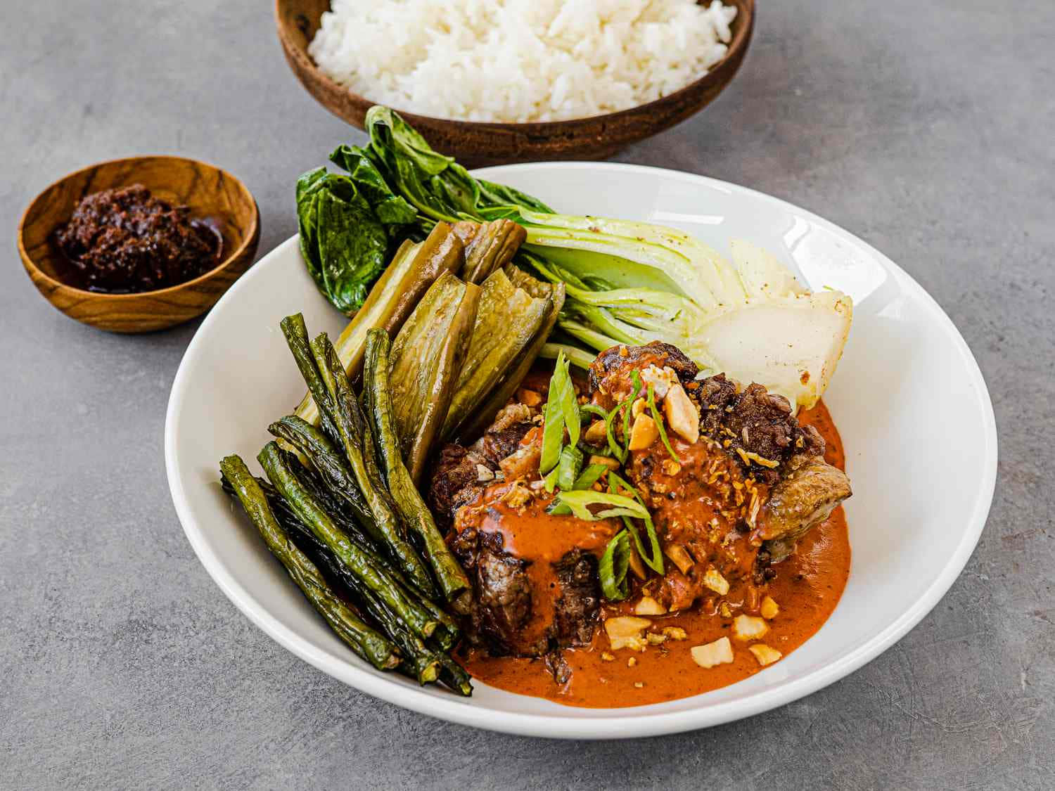 美味的菲律賓燉菜 Kare-Kare 壁紙 — 一碗充滿活力的濃郁紅咖喱，配有嫩肉、青豆和白菜，搭配白飯和深色醬汁。