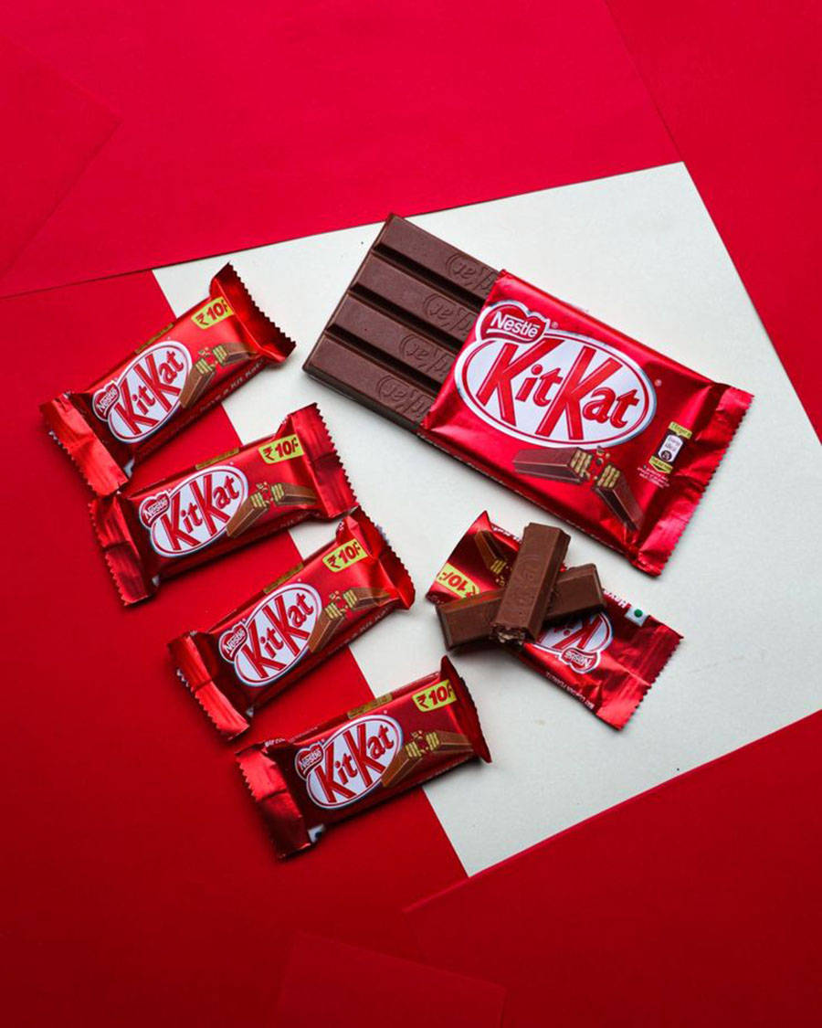 美味紅色 Kit-Kat 巧克力 壁紙 — 幾條KitKat朱古力棒和碎塊排列在鮮明的紅白幾何背景上。