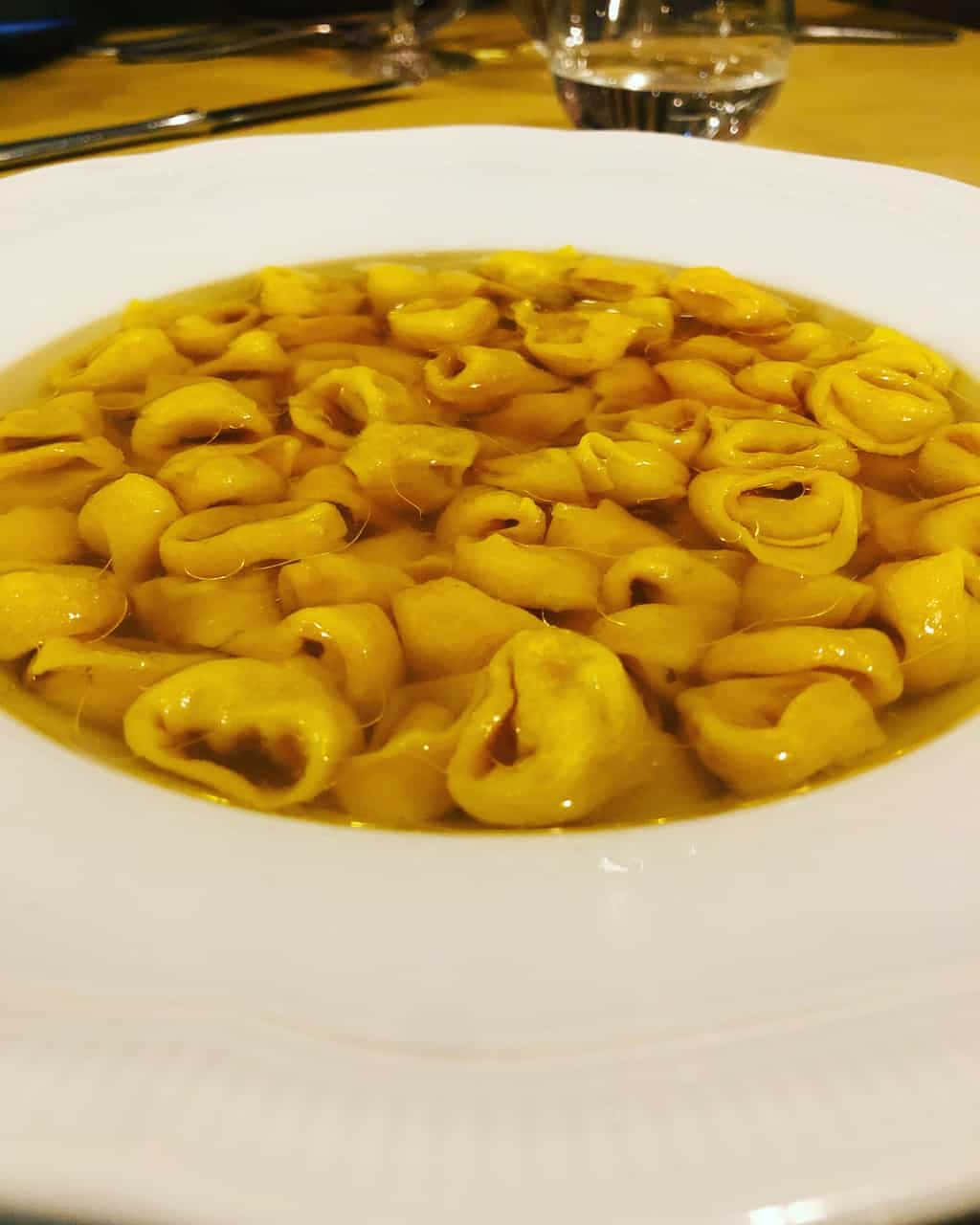 美味義式餃子湯 壁紙 — 木桌上白色碗中漂浮在金黃色濃湯中的意大利餃子特寫。