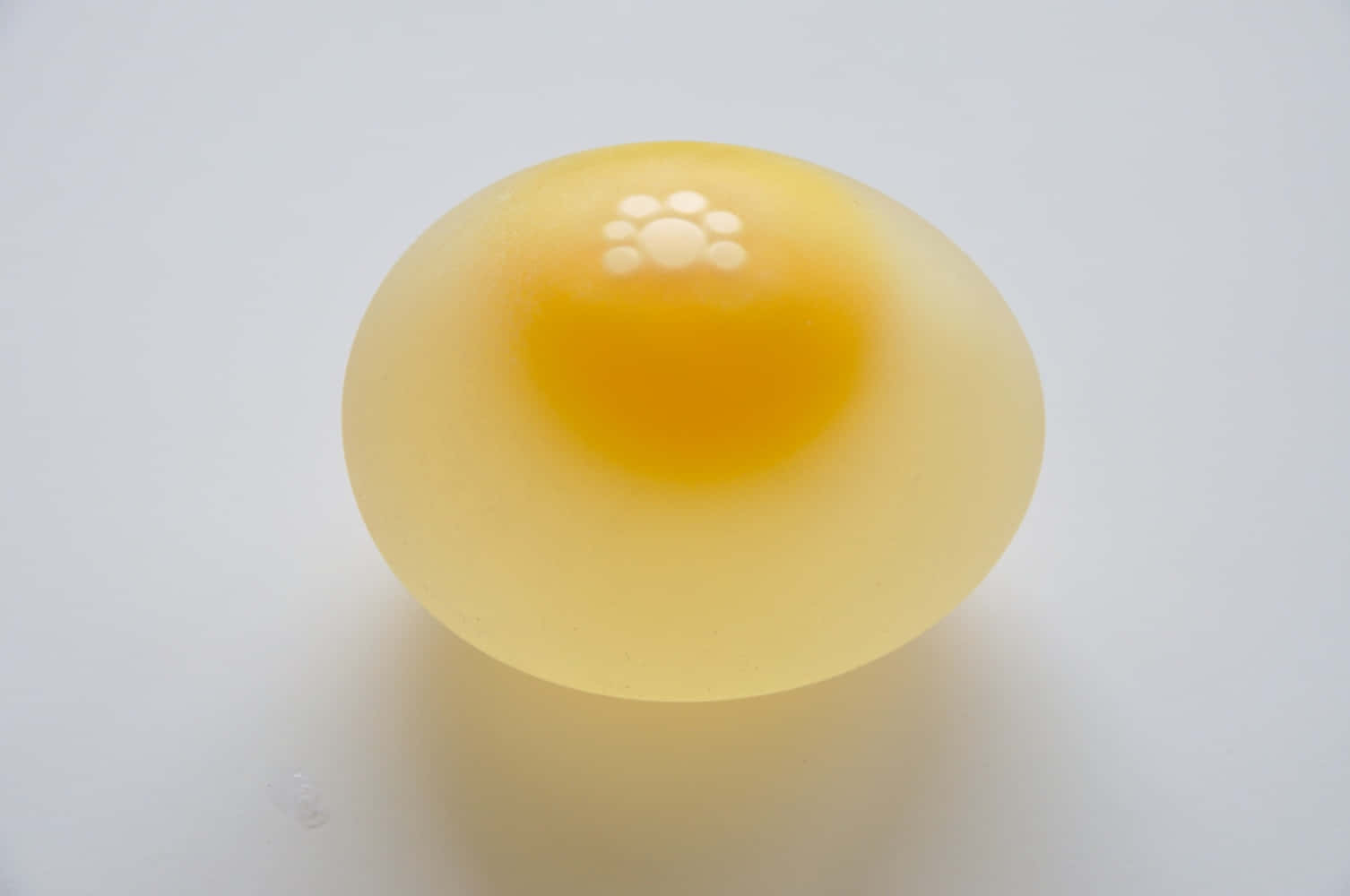 美味蛋料理 壁紙 — 一個半透明的黃色蛋黃，表面有光澤，帶有白色斑點，位於純白色背景中央。