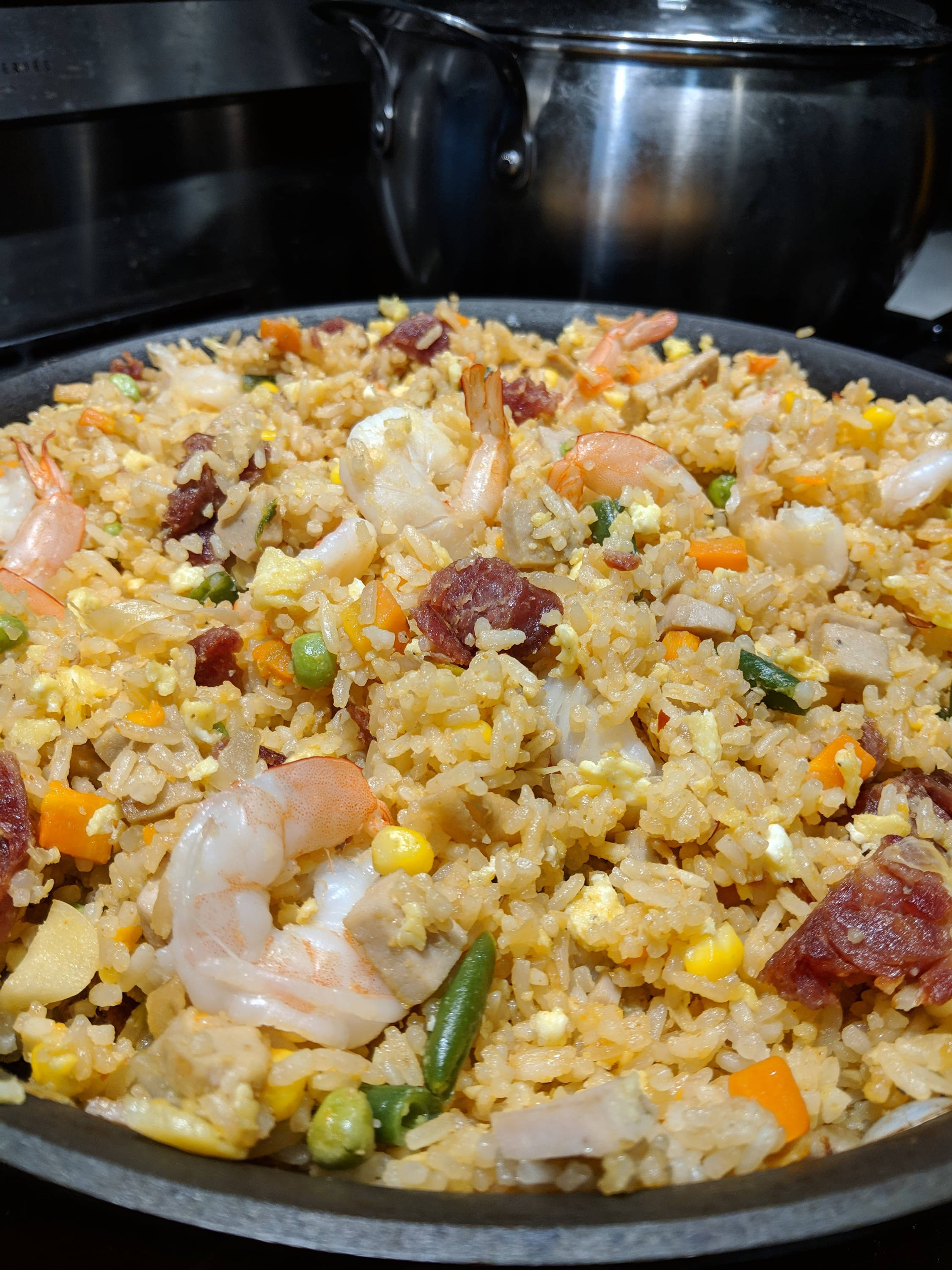 美味蝦仁炒飯 壁紙 — 黑鑊中金黃色炒飯配蝦仁、粟米、青豆和香腸的特寫，置於爐灶上。