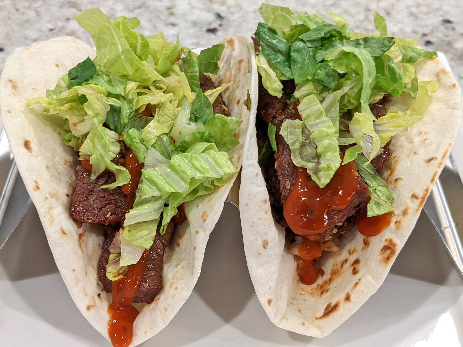 美味韓式醬油牛肉塔可 壁紙 — 兩個軟玉米餅夾著調味肉、新鮮生菜和鮮紅色醬汁，並排放在白色碟子上。