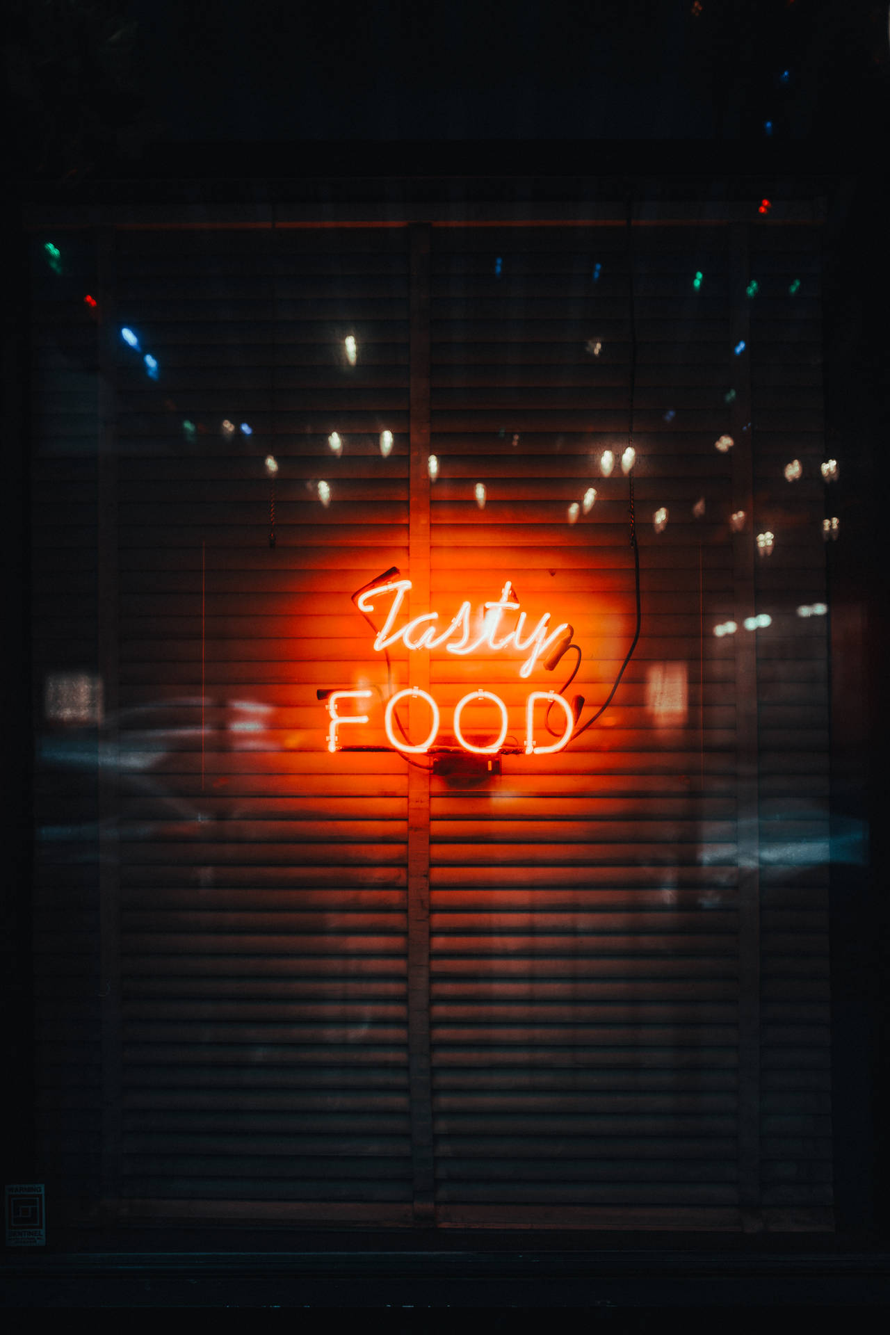 夜間穿過關閉的百葉窗發光的霓虹燈牌，上面寫著 tasty food。