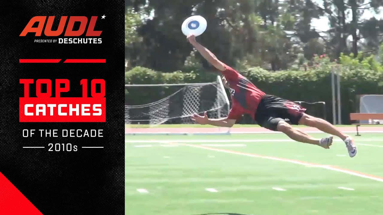 美國 Ultimate Disc 聯盟最佳 Ultimate Frisbee 背景海報 壁紙 — 一名身穿紅黑相間服裝的男性運動員在綠色場地上騰空躍起，單手接住一個白色飛盤。