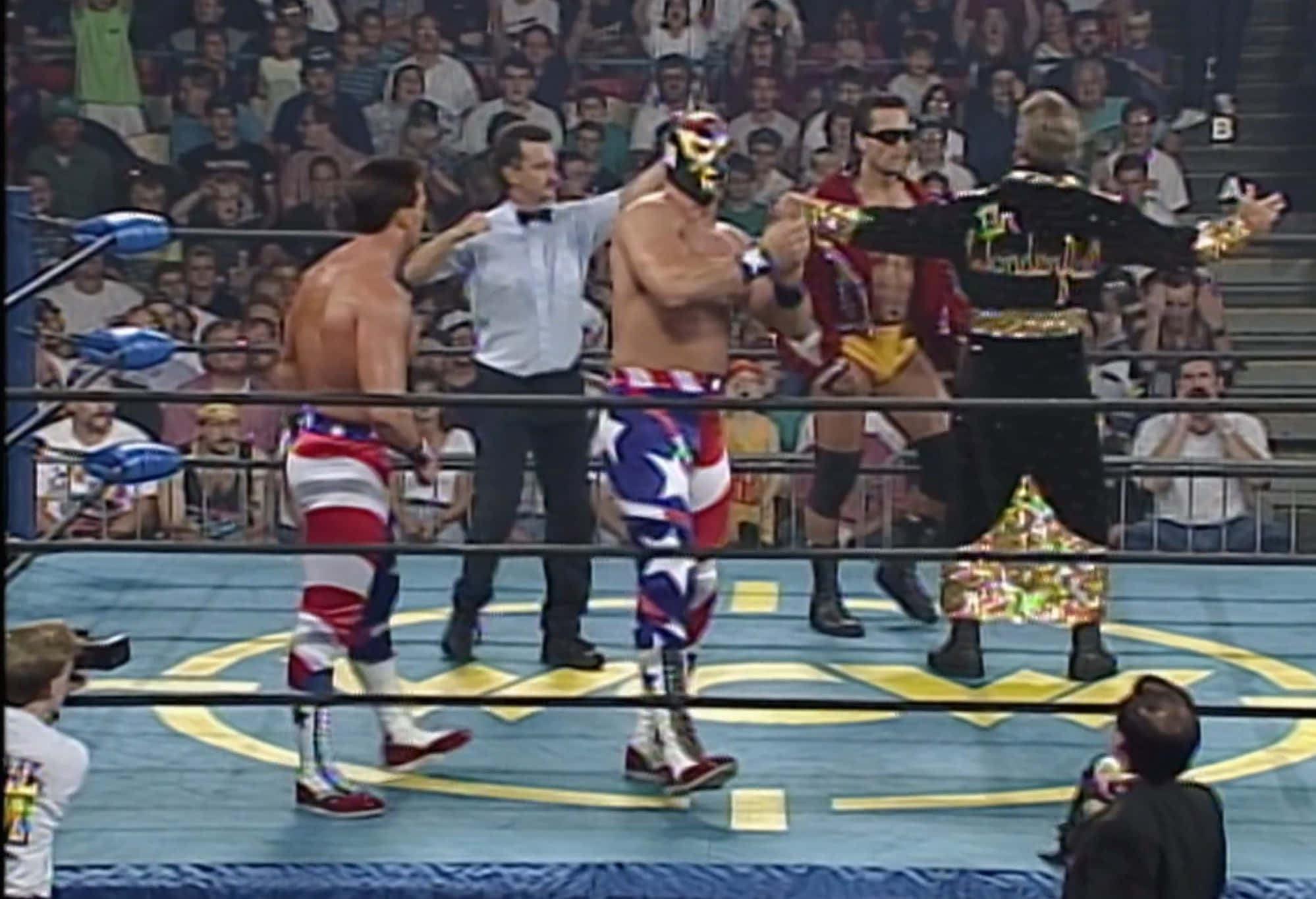 美國 WWE 摔角手 The Patriot WCW 1994 壁紙 — 身穿色彩繽紛服裝的摔角手在擂台上對峙，背景有裁判和歡呼的人群。