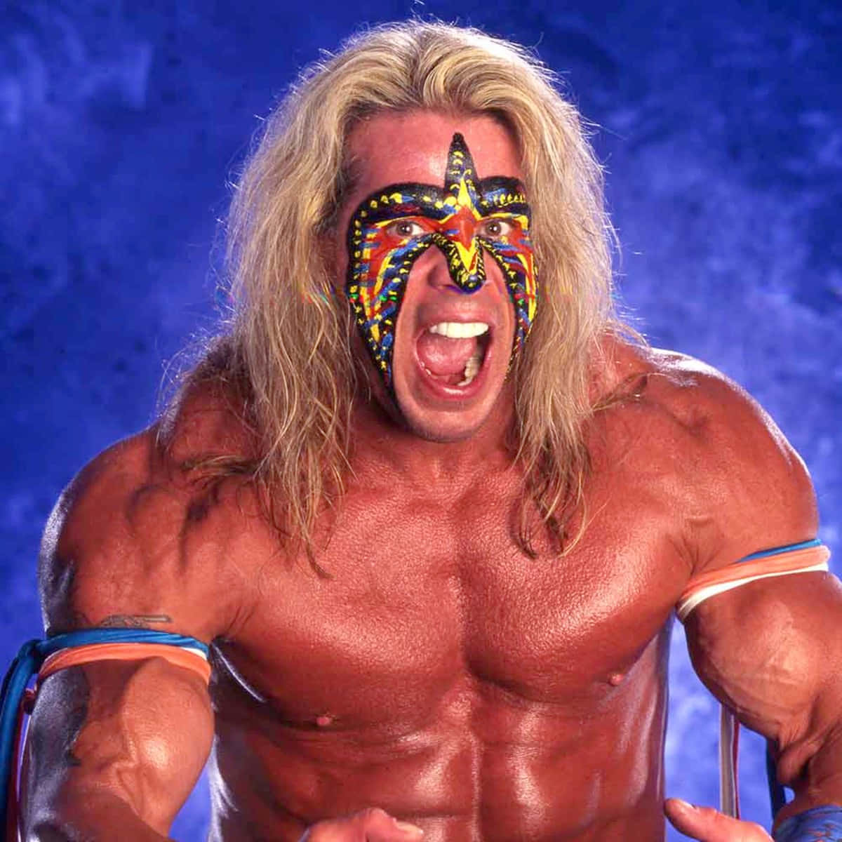 美國 WWE 摔角手 Ultimate Warrior 頭部特寫復古風格 壁紙 — 一位肌肉發達、留著金色長髮、臉上畫著彩色星星圖案的摔角手，在深藍色背景下猛烈咆哮。