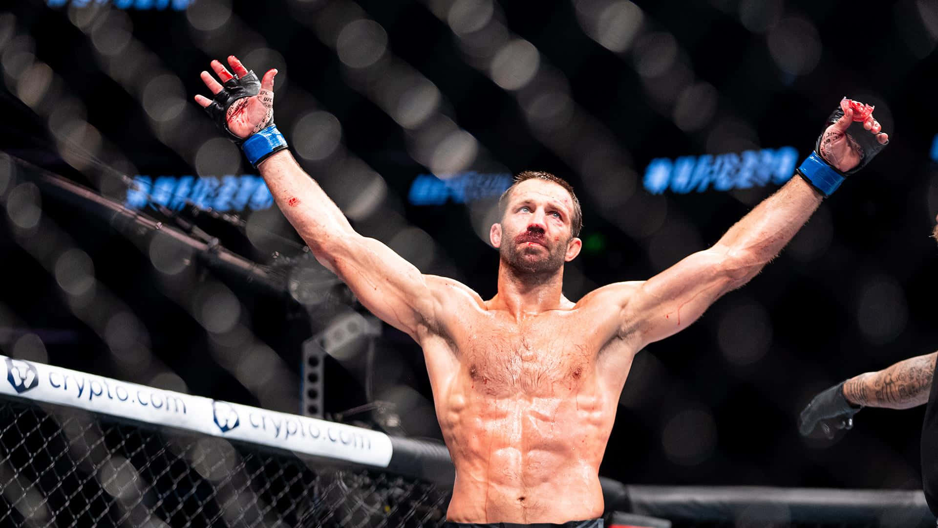 美國MMA運動員盧克·羅克霍德UFC 278 壁紙 — 一位勝利的混合武術家在昏暗的八角籠內高舉雙臂慶祝勝利，身後是模糊的籠網。