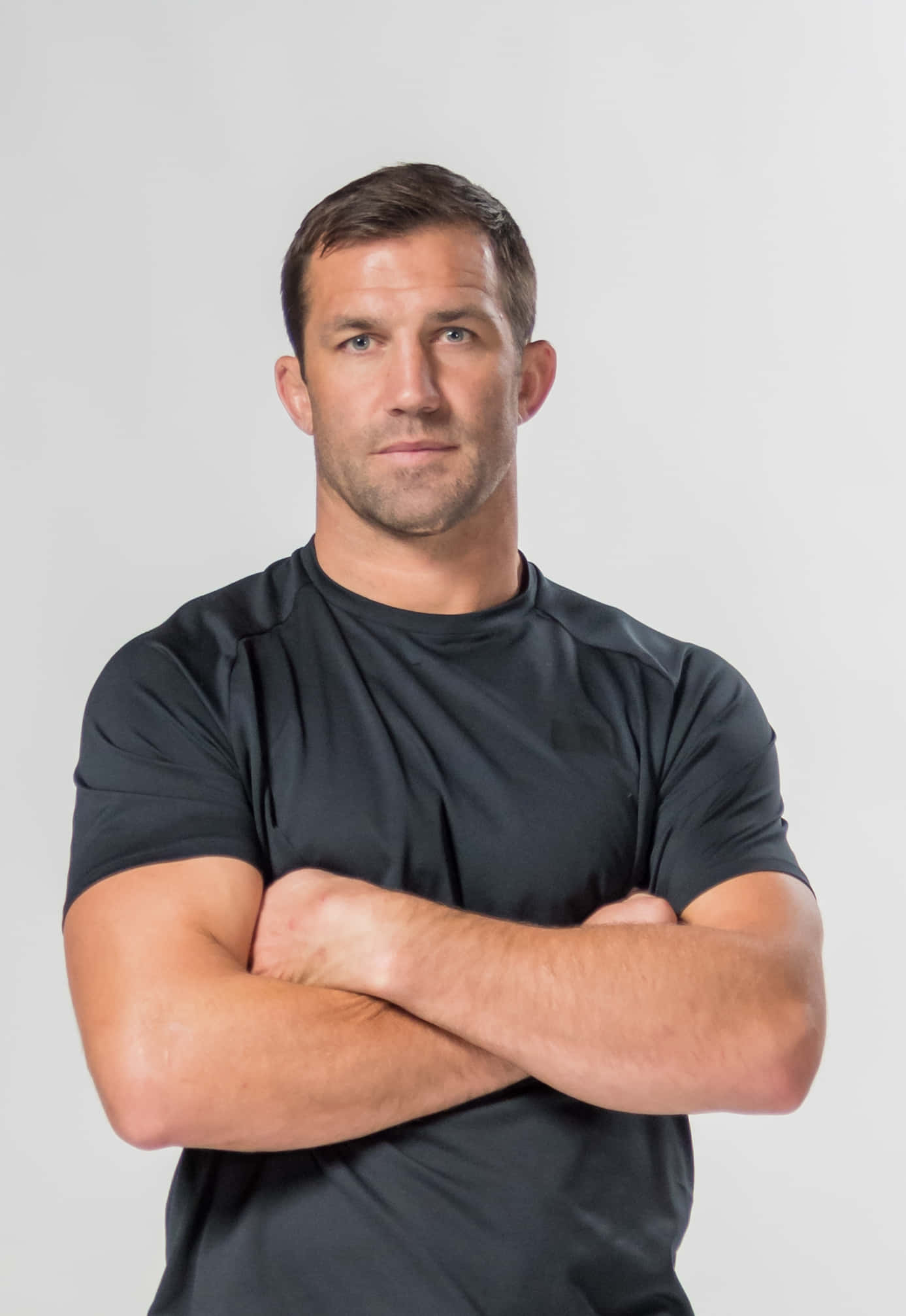 美國MMA運動員盧克·羅克霍德八角籠戰士肖像 壁紙 — 一個肌肉發達的男人穿著黑色T恤，雙臂交叉，自信地站在純灰色背景前。