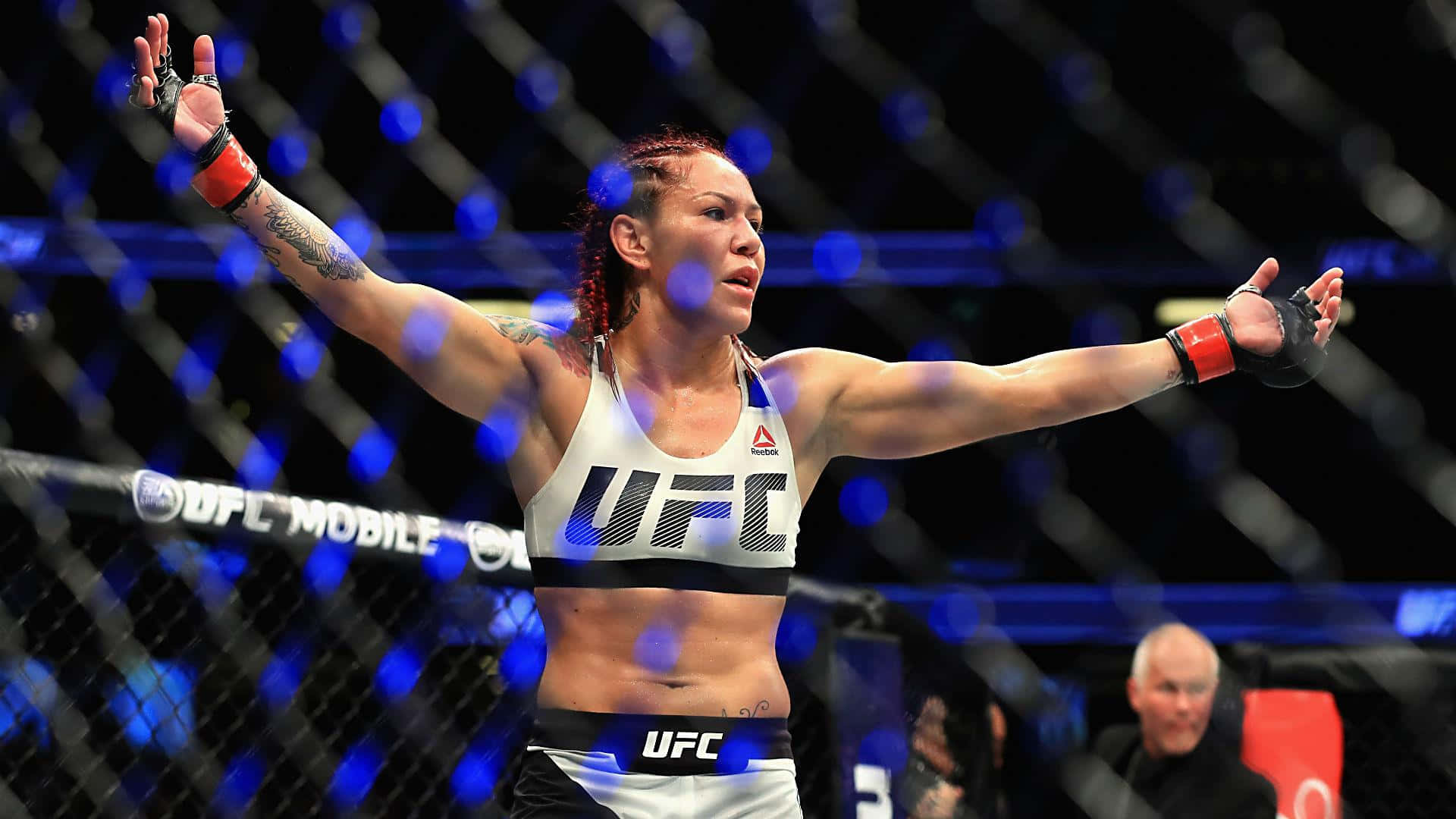 美國MMA選手Cris Cyborg 2017賽事慶祝照 壁紙 — 一位女性UFC拳手在燈光明亮的八角籠內高舉雙臂慶祝勝利。